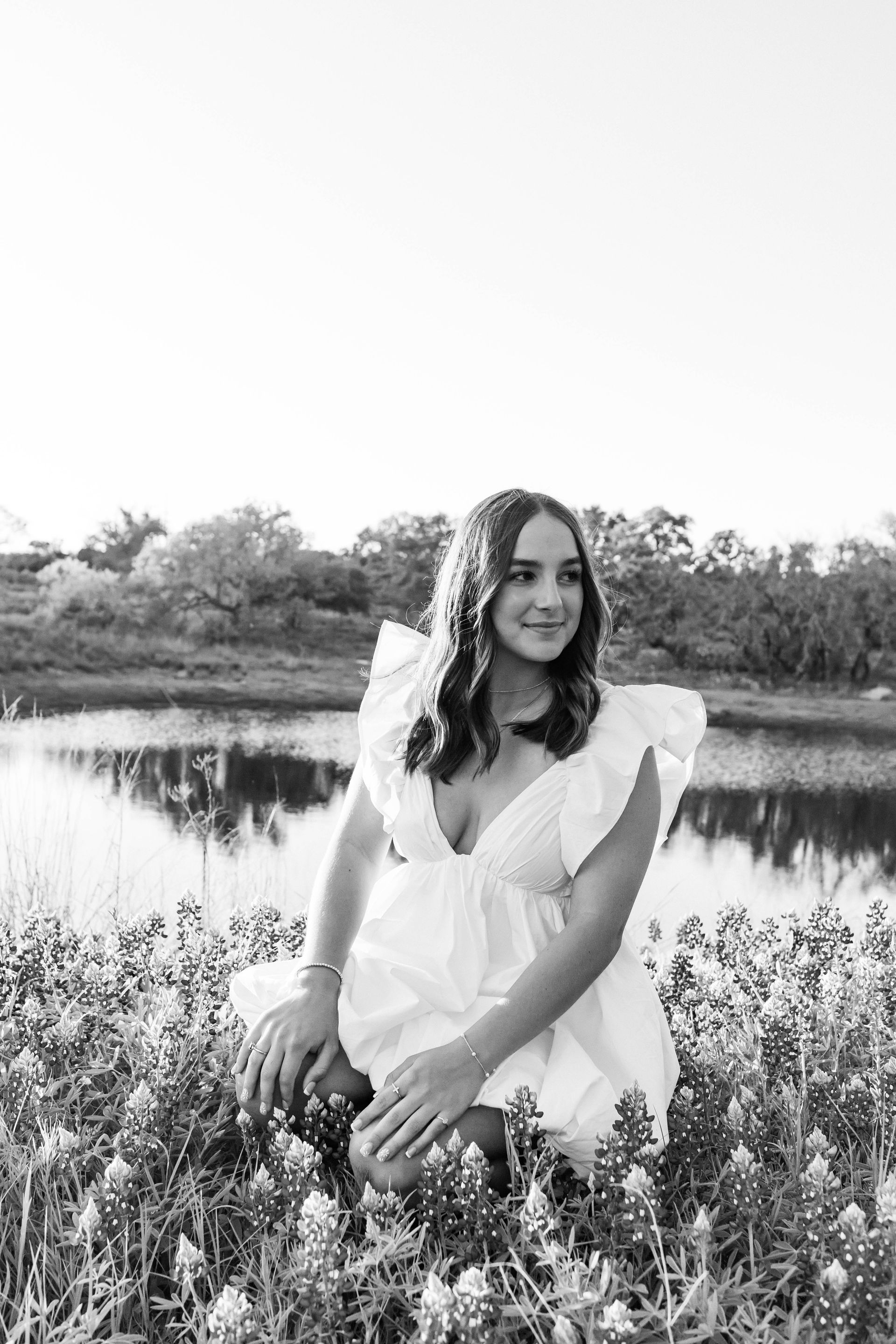 A woman in a white dress is kneeling in a field of flowers.