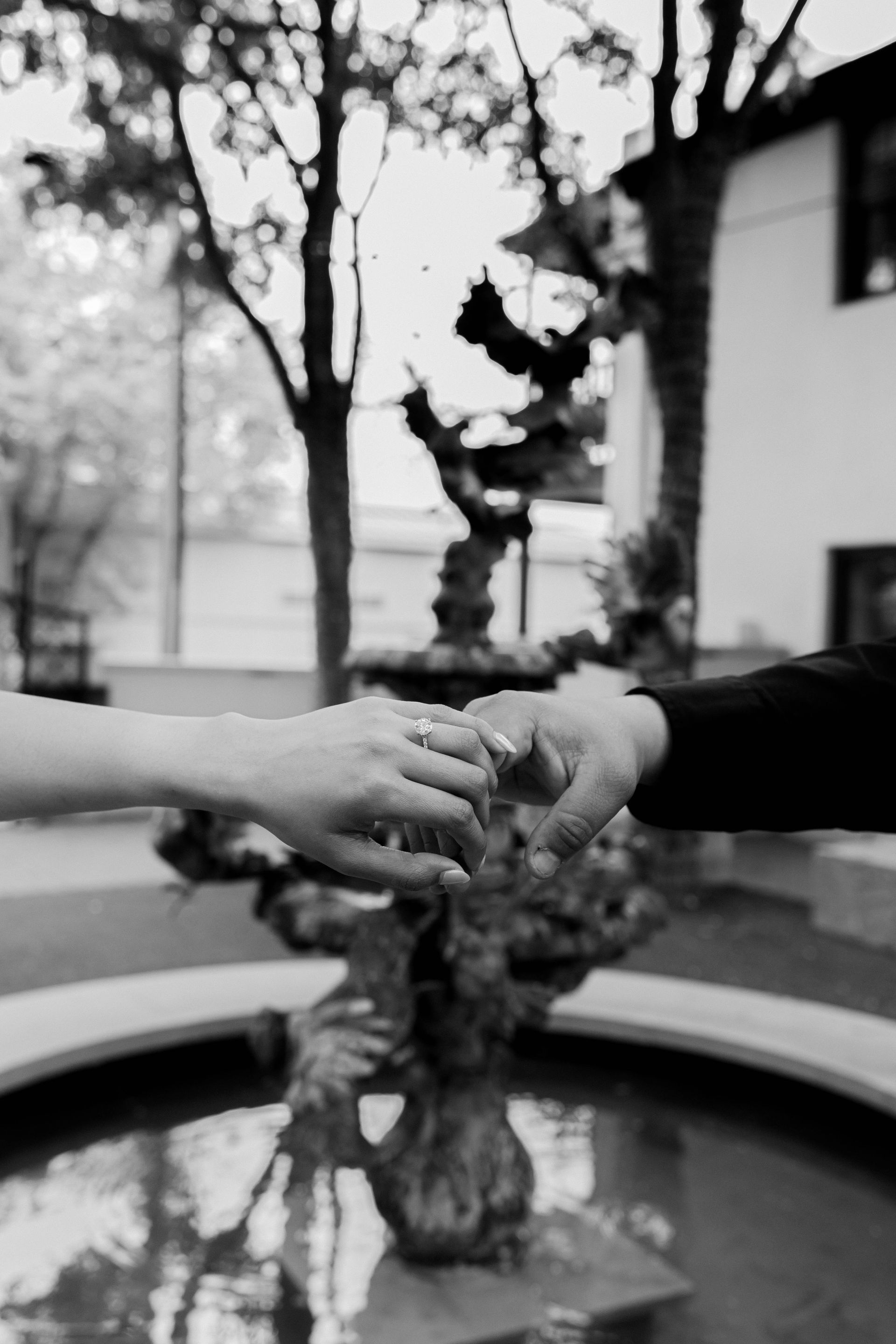 A black and white photo of a couple holding hands in front of a fountain.