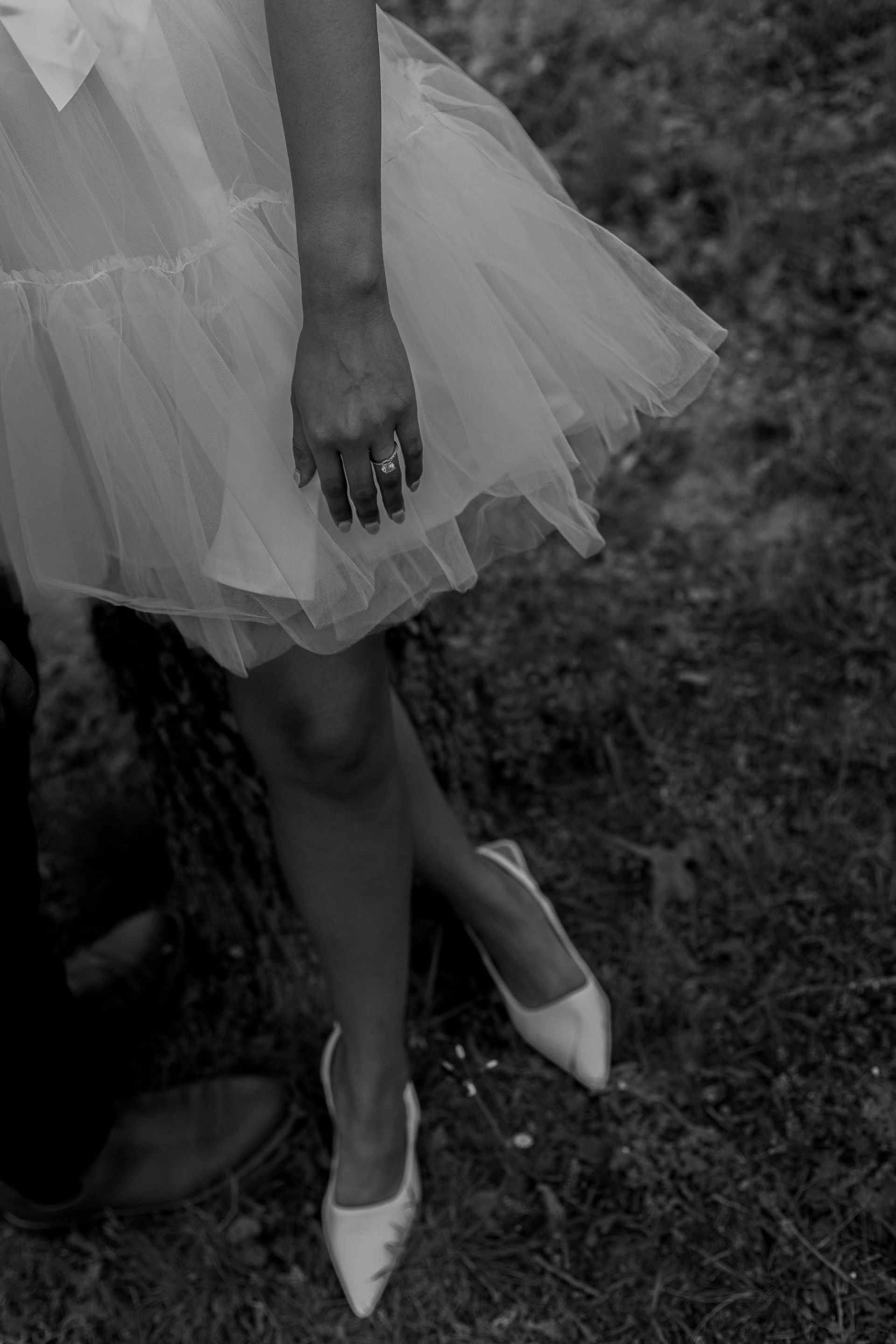 A woman in a white dress and white shoes is standing next to a tree trunk.