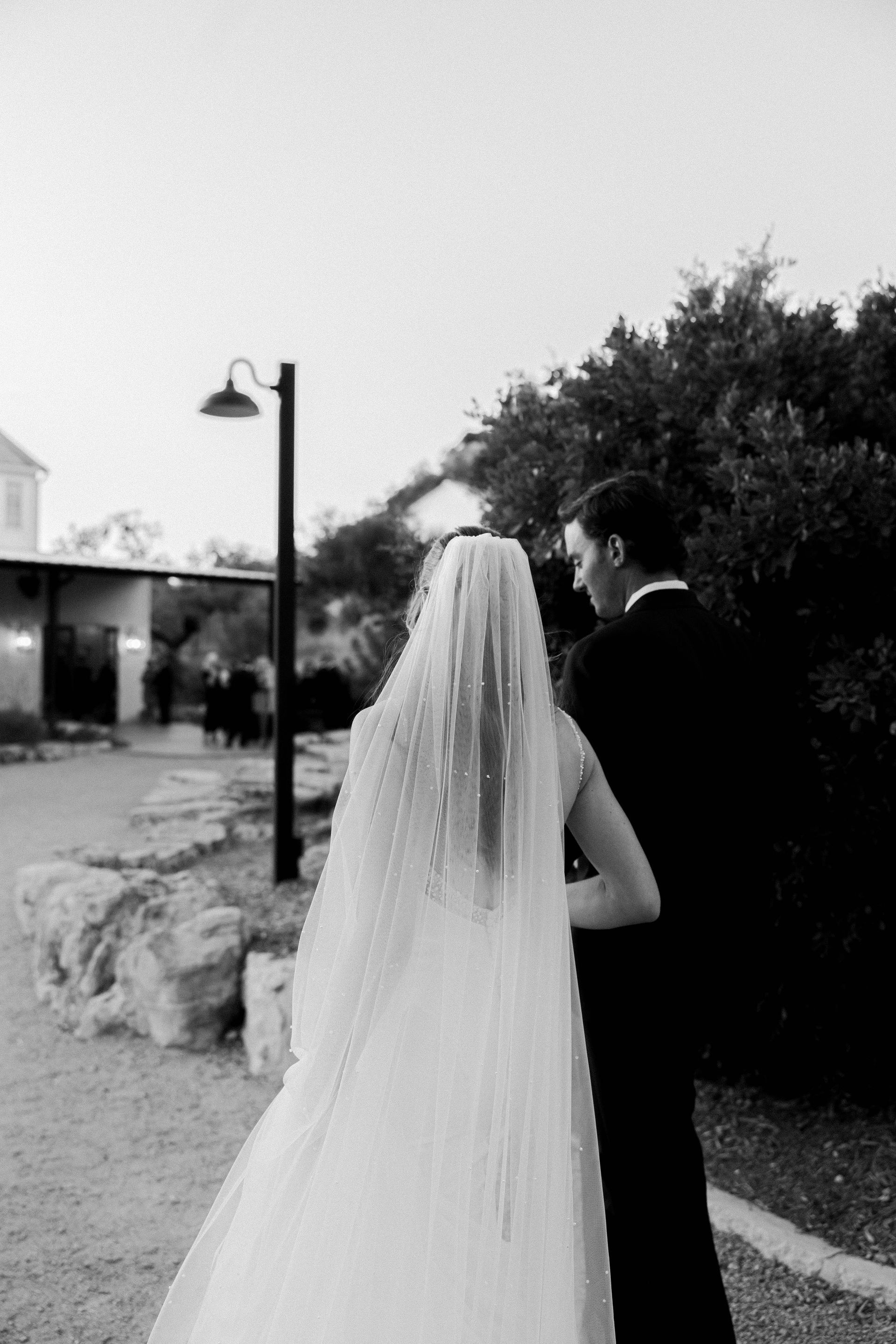 A black and white photo of a bride and groom walking down a path.