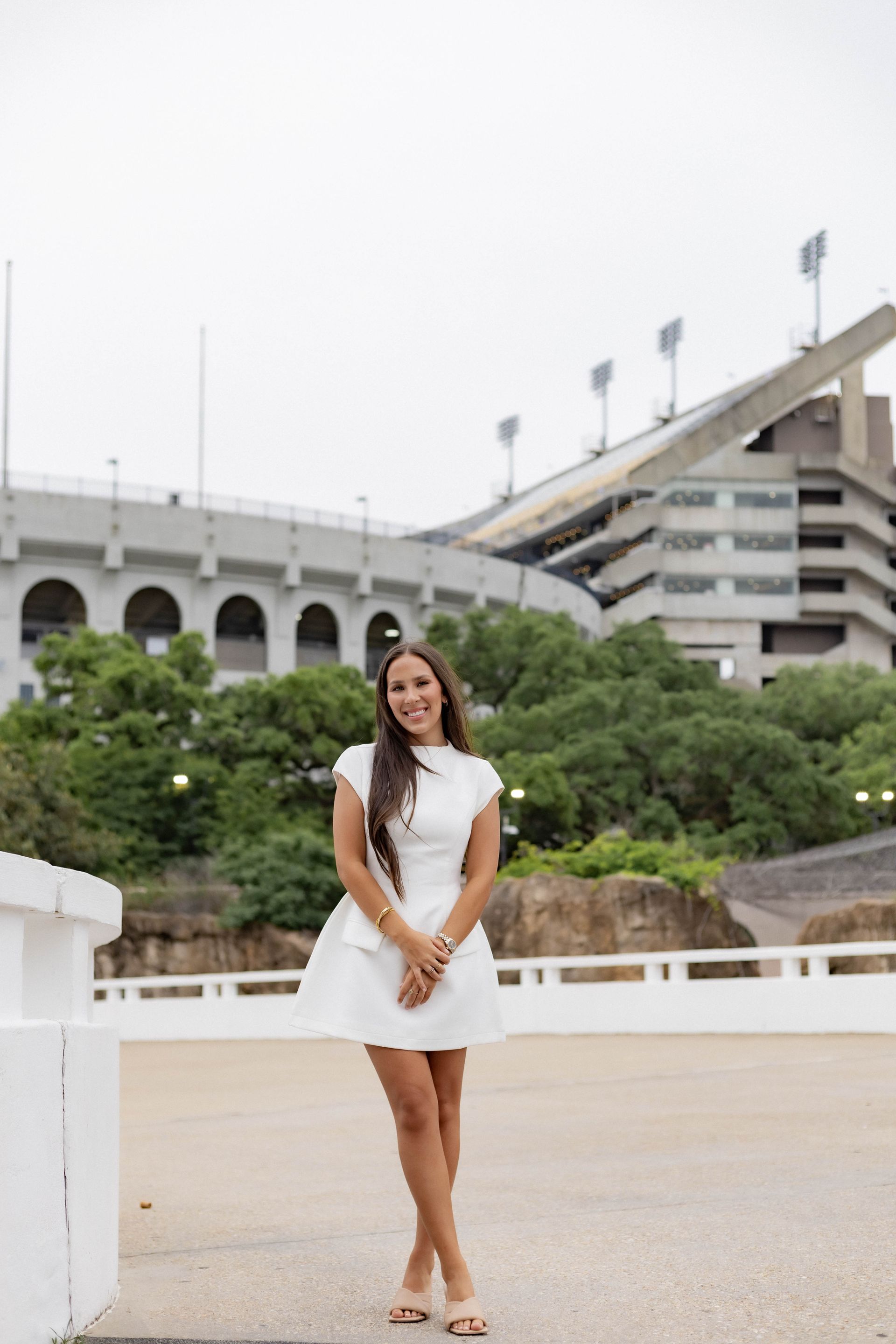 A woman in a white dress is standing in front of a stadium.