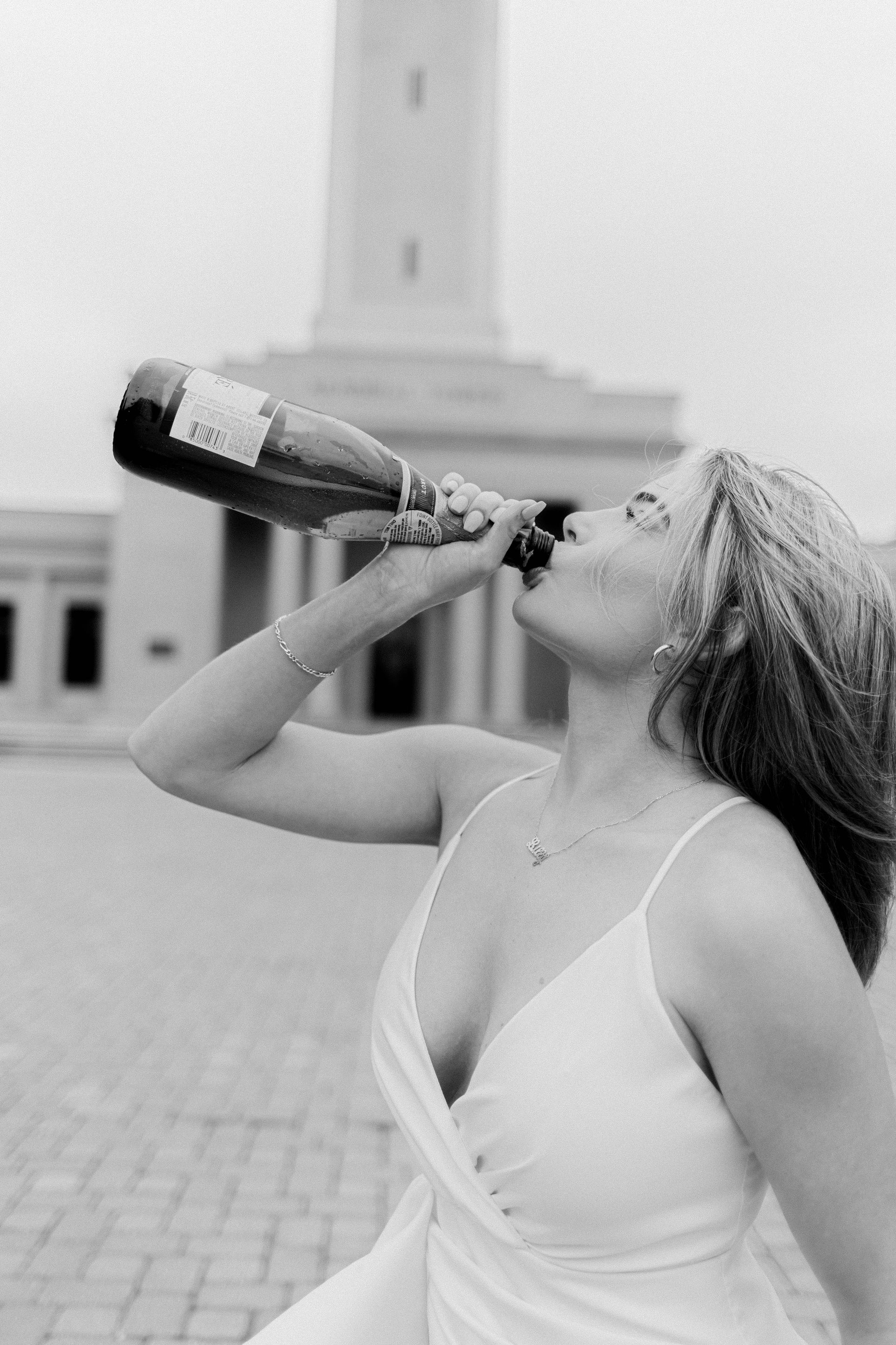 A woman in a white dress is drinking from a bottle of champagne.