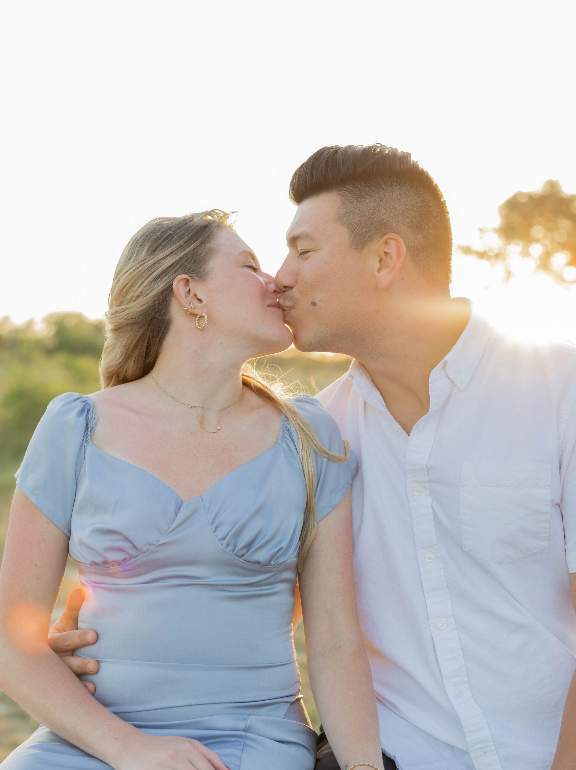 A man and a woman are kissing while sitting next to each other in a field.