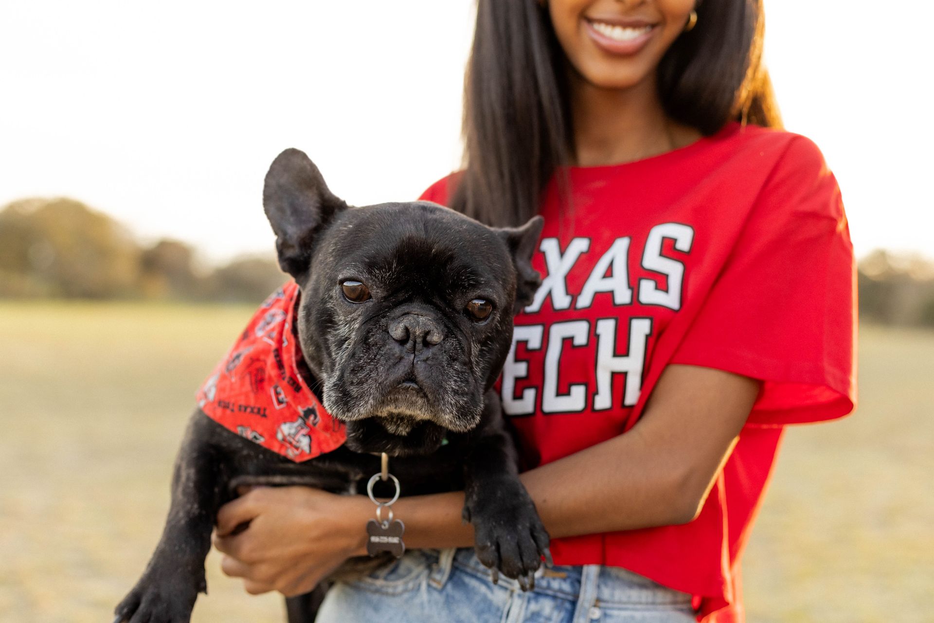 A woman in a red shirt is holding a black dog.