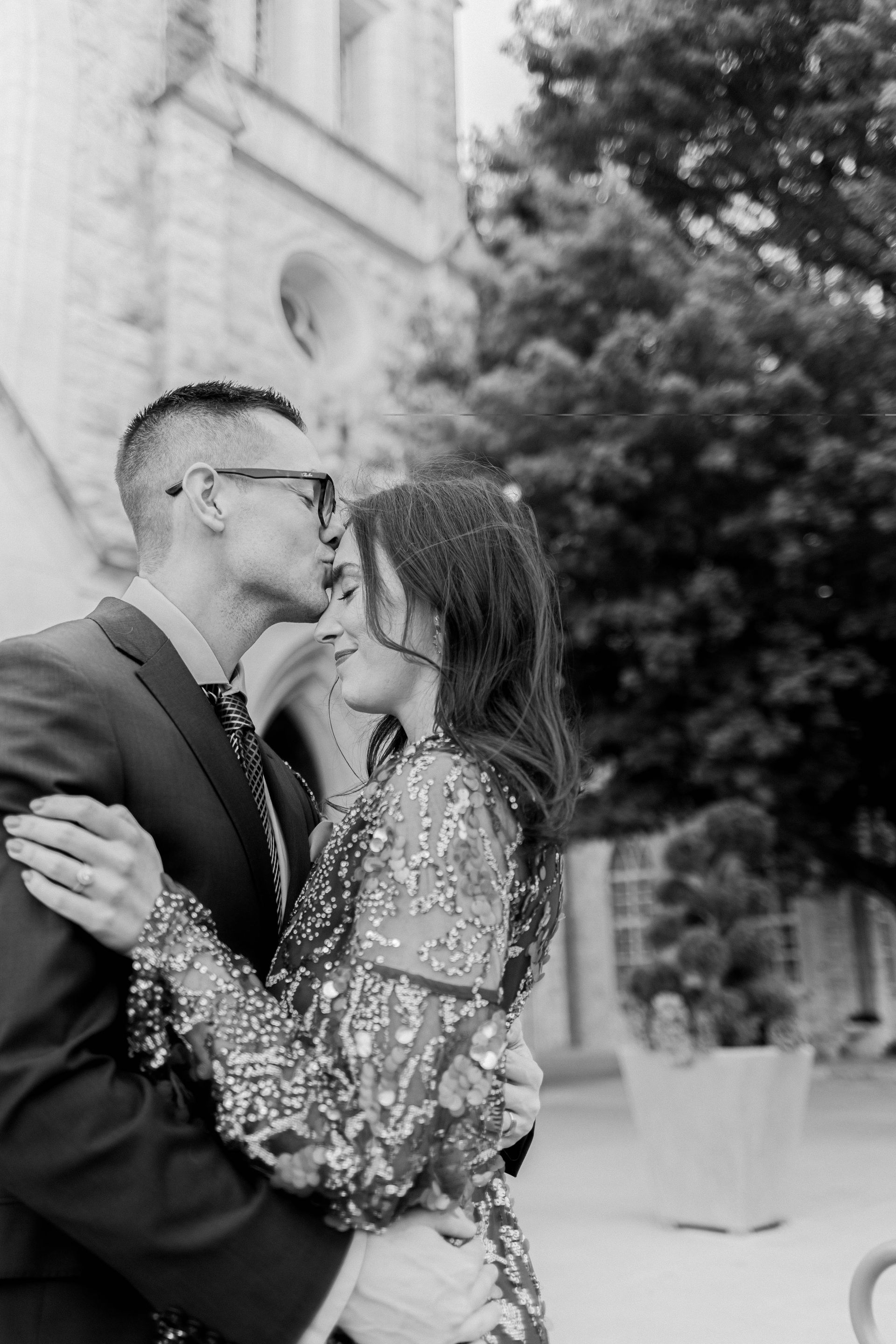 A black and white photo of a man and woman kissing in front of a building.