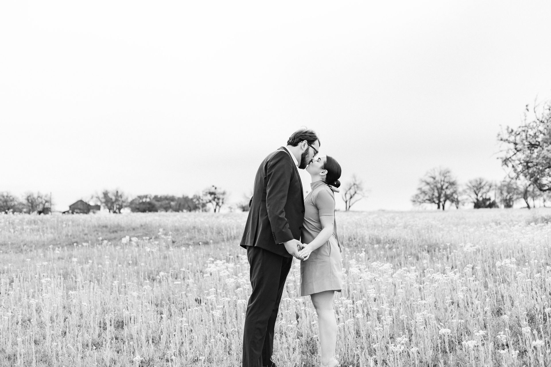 A black and white photo of a man and woman kissing in a field.