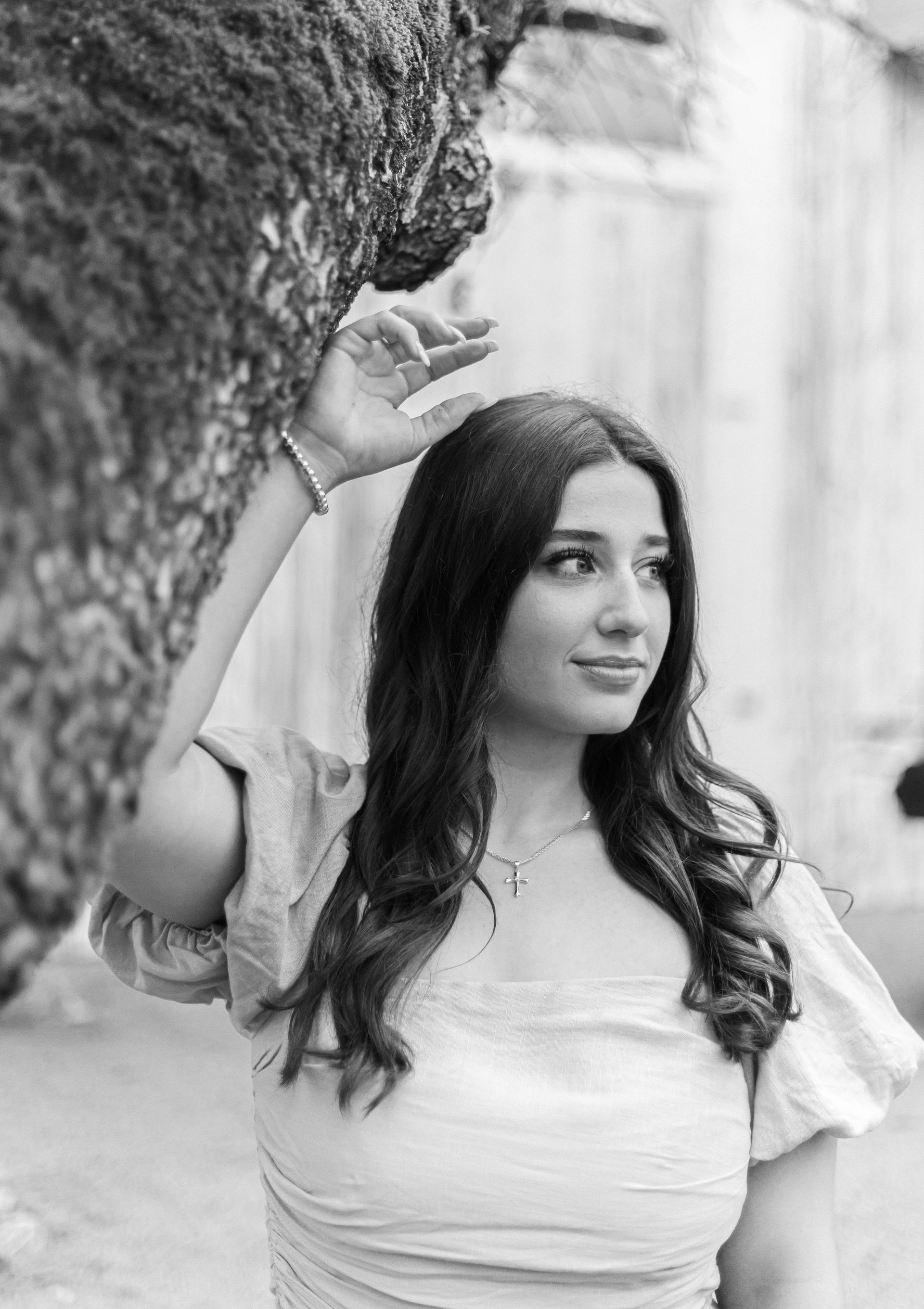 A black and white photo of a woman standing next to a tree.