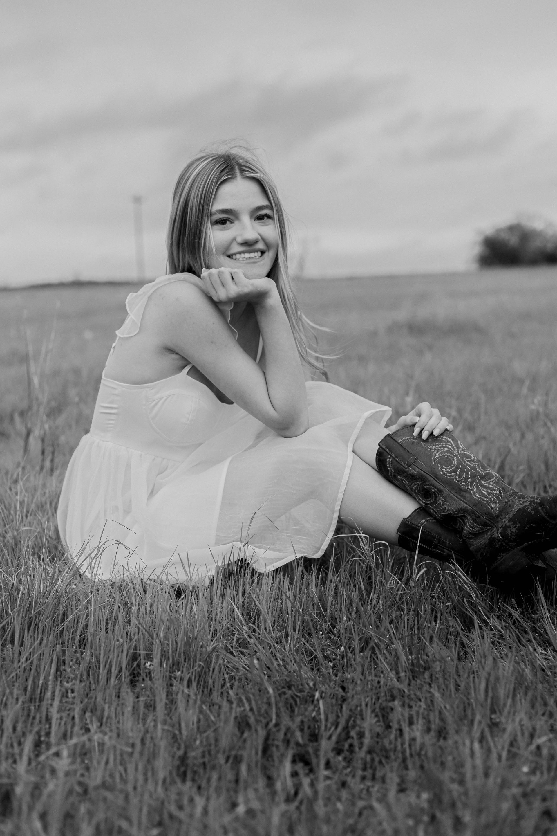 A black and white photo of a woman in a white dress sitting in a field.