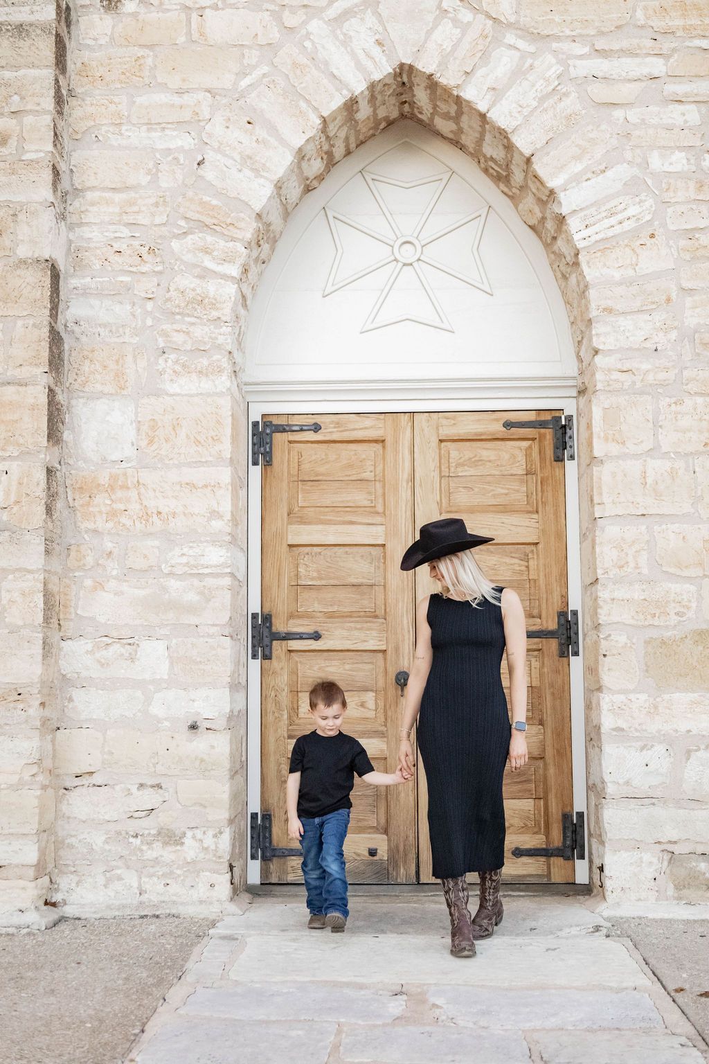 A woman and a child are holding hands in front of a church door.