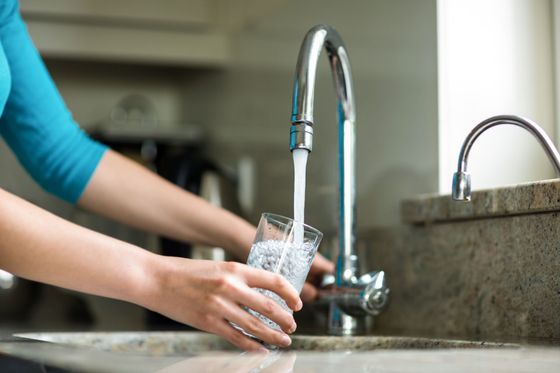 A woman is filling a glass of water from a faucet.