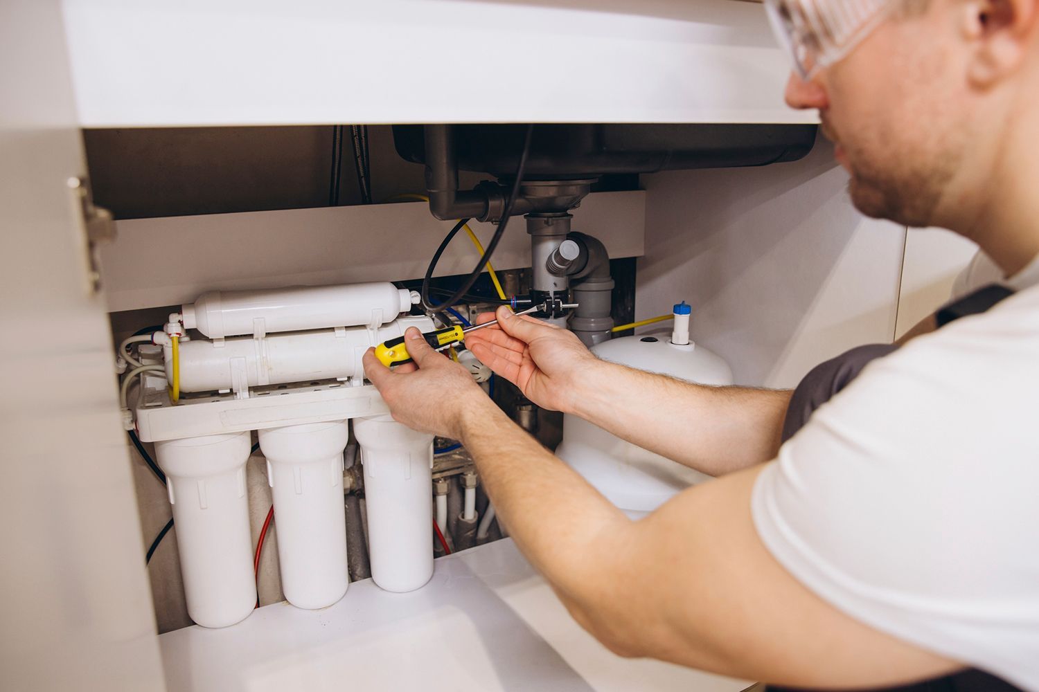 A plumber installing a water softening system under the kitchen sink.