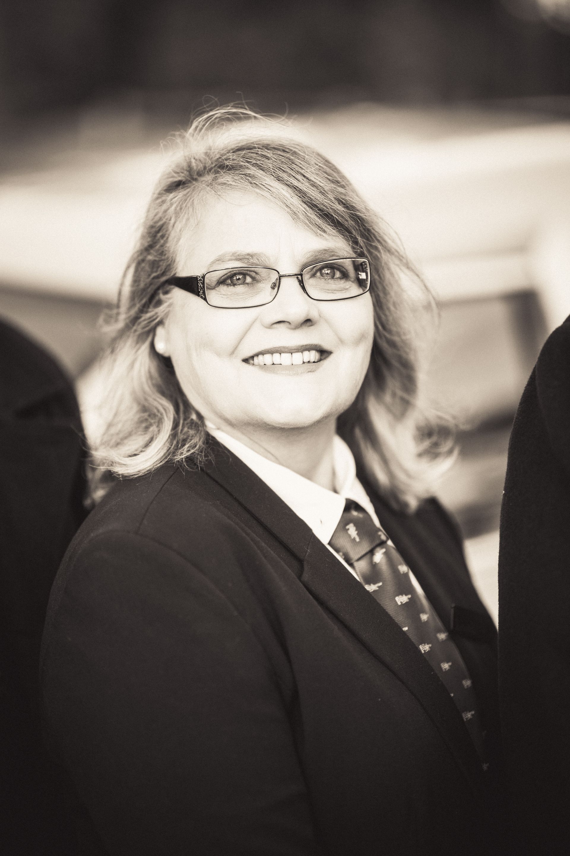 A woman wearing glasses and a suit and tie is smiling in a black and white photo.