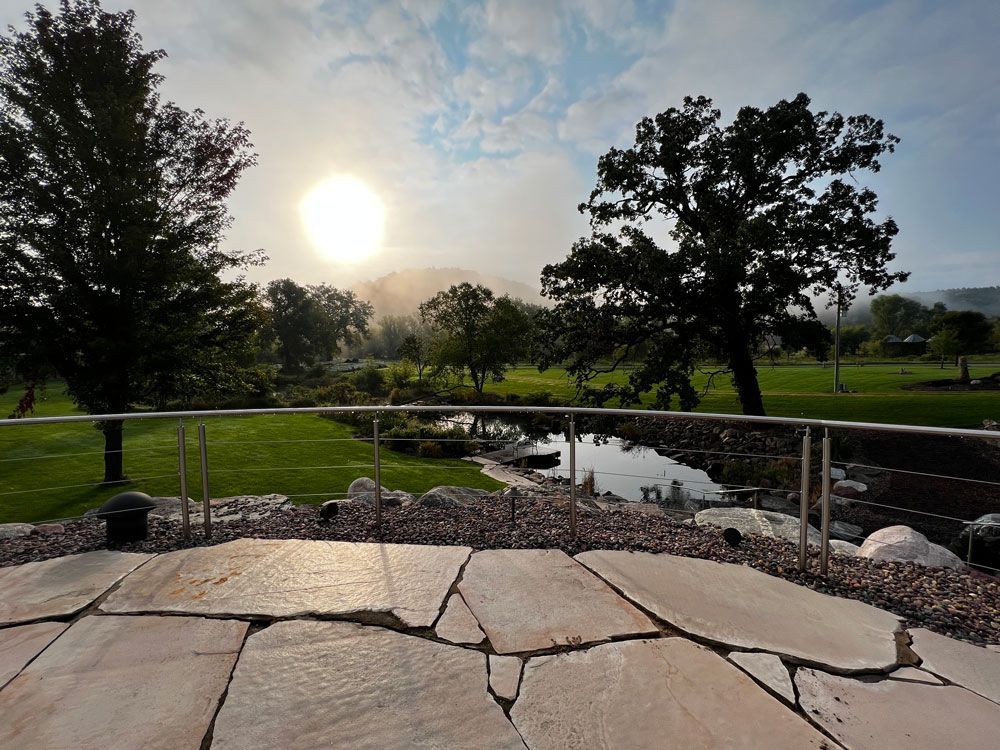 Stone patio overlooking a pond, trees, and a sunlit misty landscape.