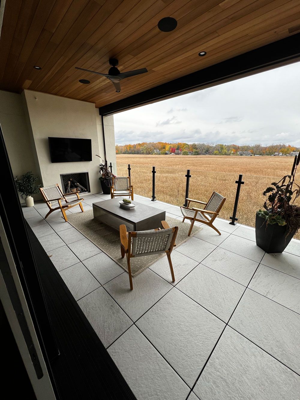 Patio with seating, fireplace, and view of a field under an overcast sky.