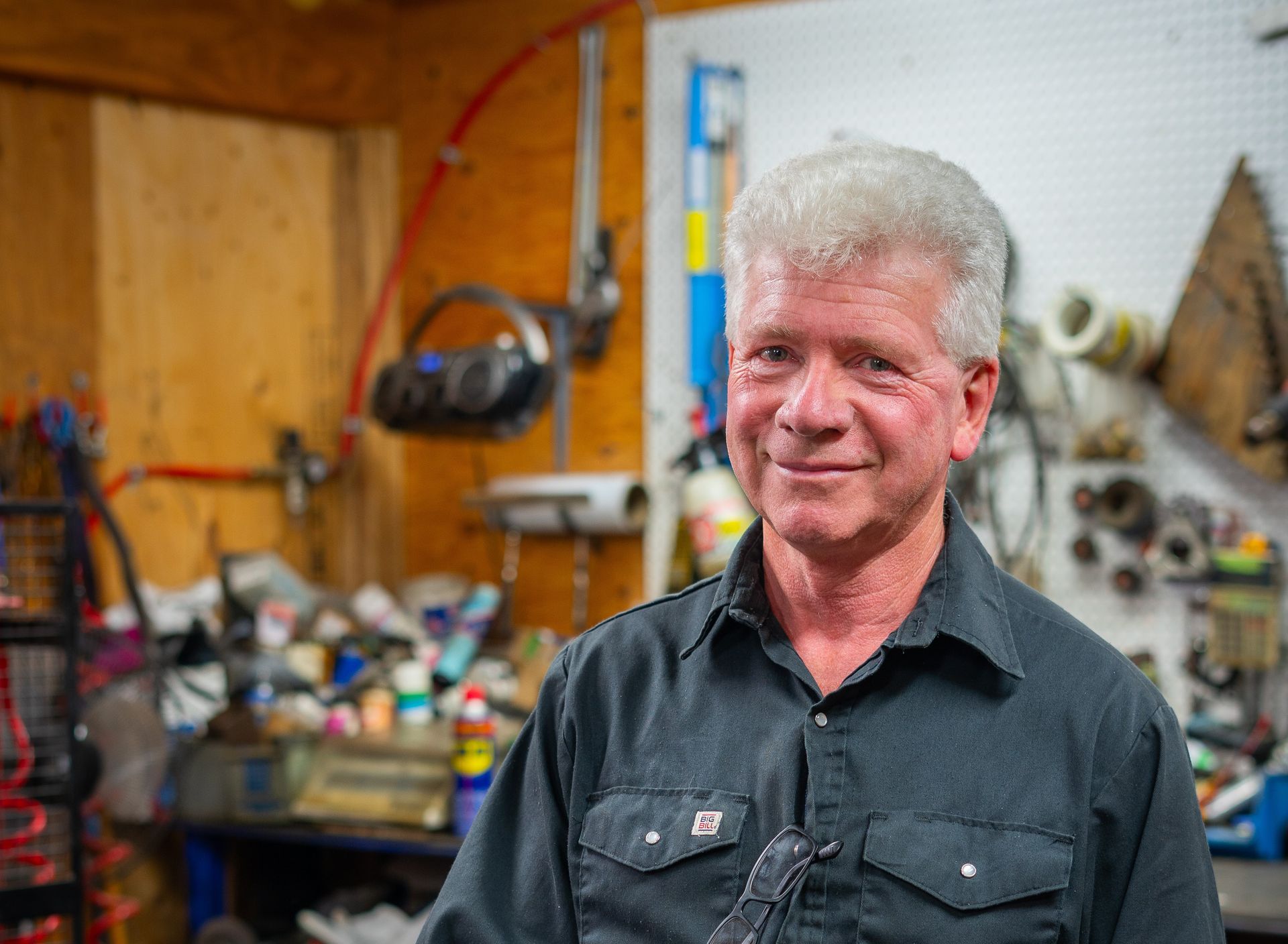 Un homme est debout dans un garage, tenant un tuyau et souriant.