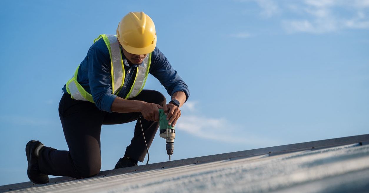 A man is using a drill to install a metal roof.