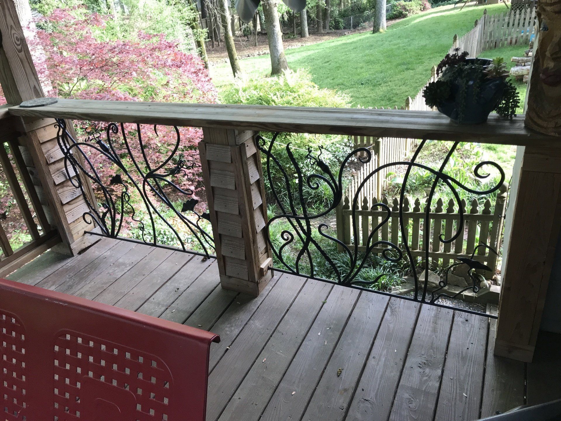 A wooden porch with a wrought iron railing and a red chair.