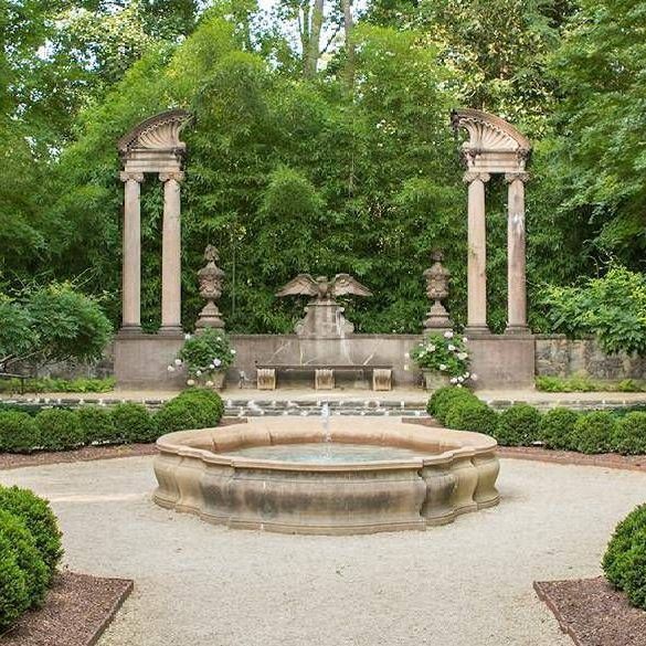 There is a fountain in the middle of the garden surrounded by trees.