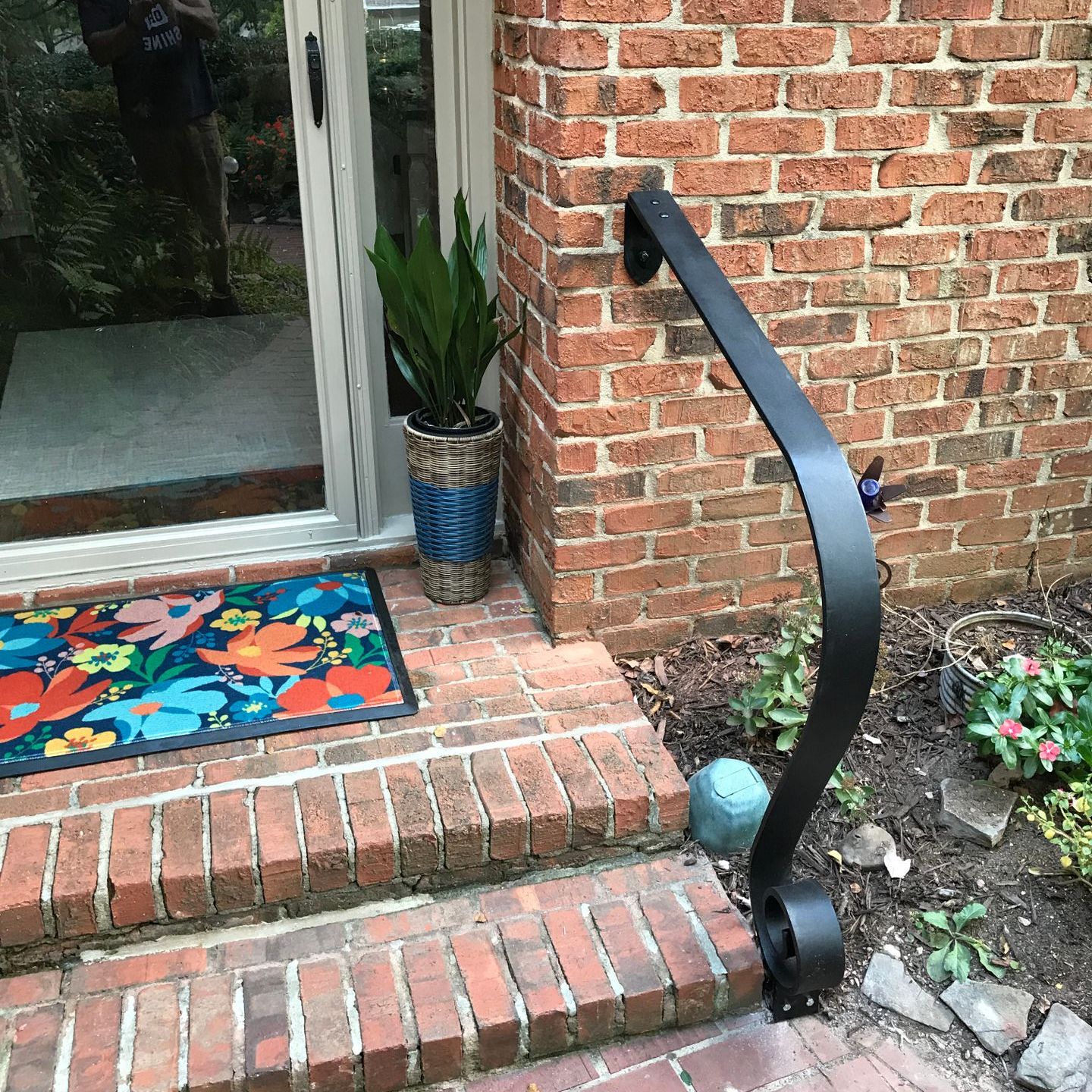 A black railing is sitting on a brick porch next to a sliding glass door.