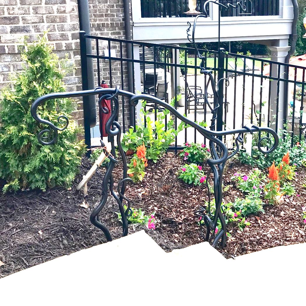 A wrought iron railing is surrounded by flowers and a fence.