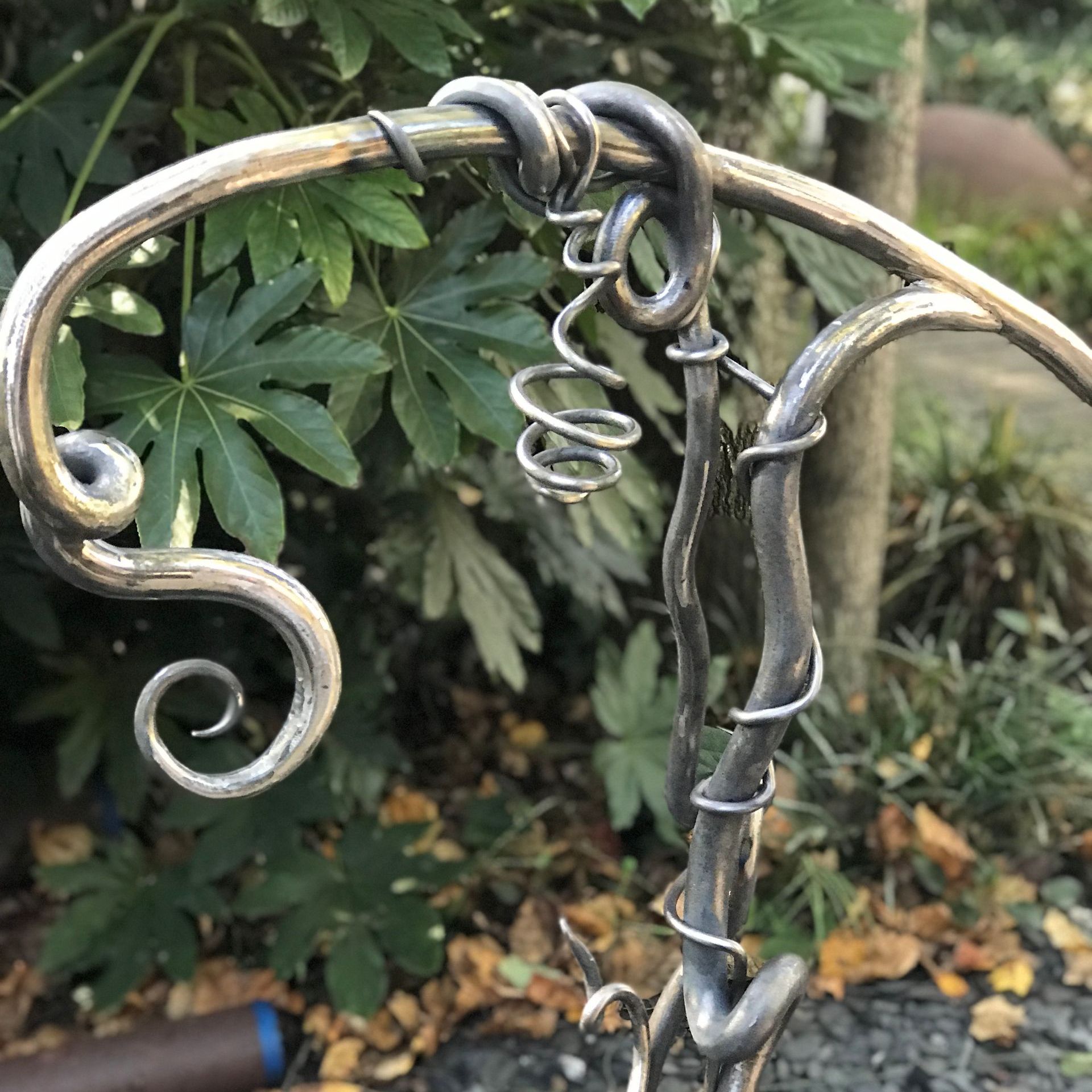 A close up of a wrought iron chair with leaves in the background.