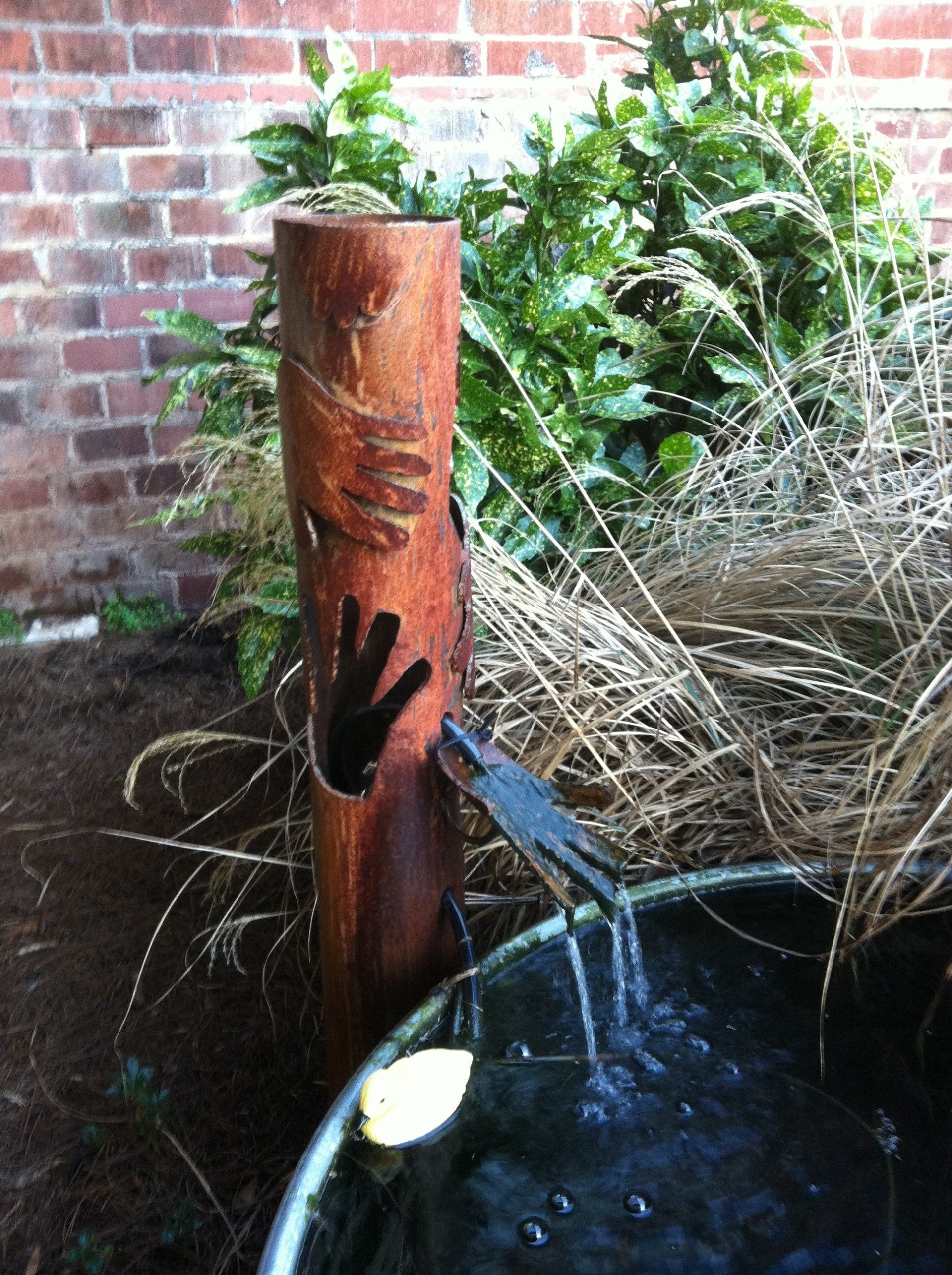 A wooden pole with a hand carved into it is sitting next to a bucket of water.