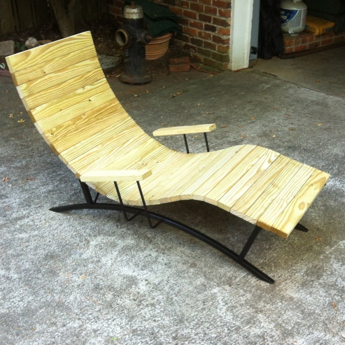 A wooden chaise lounge is sitting on the ground in front of a brick building.