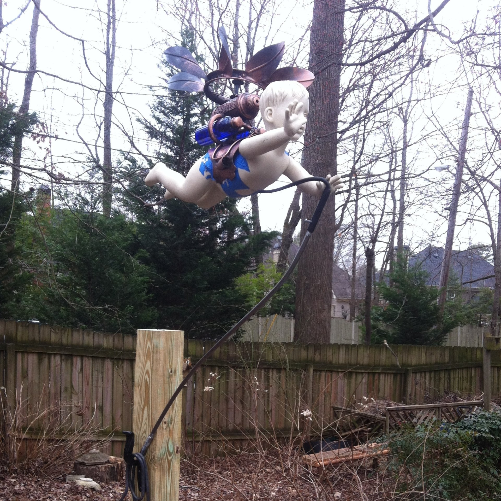 A statue of a steampunk baby with wings is flying over a wooden fence