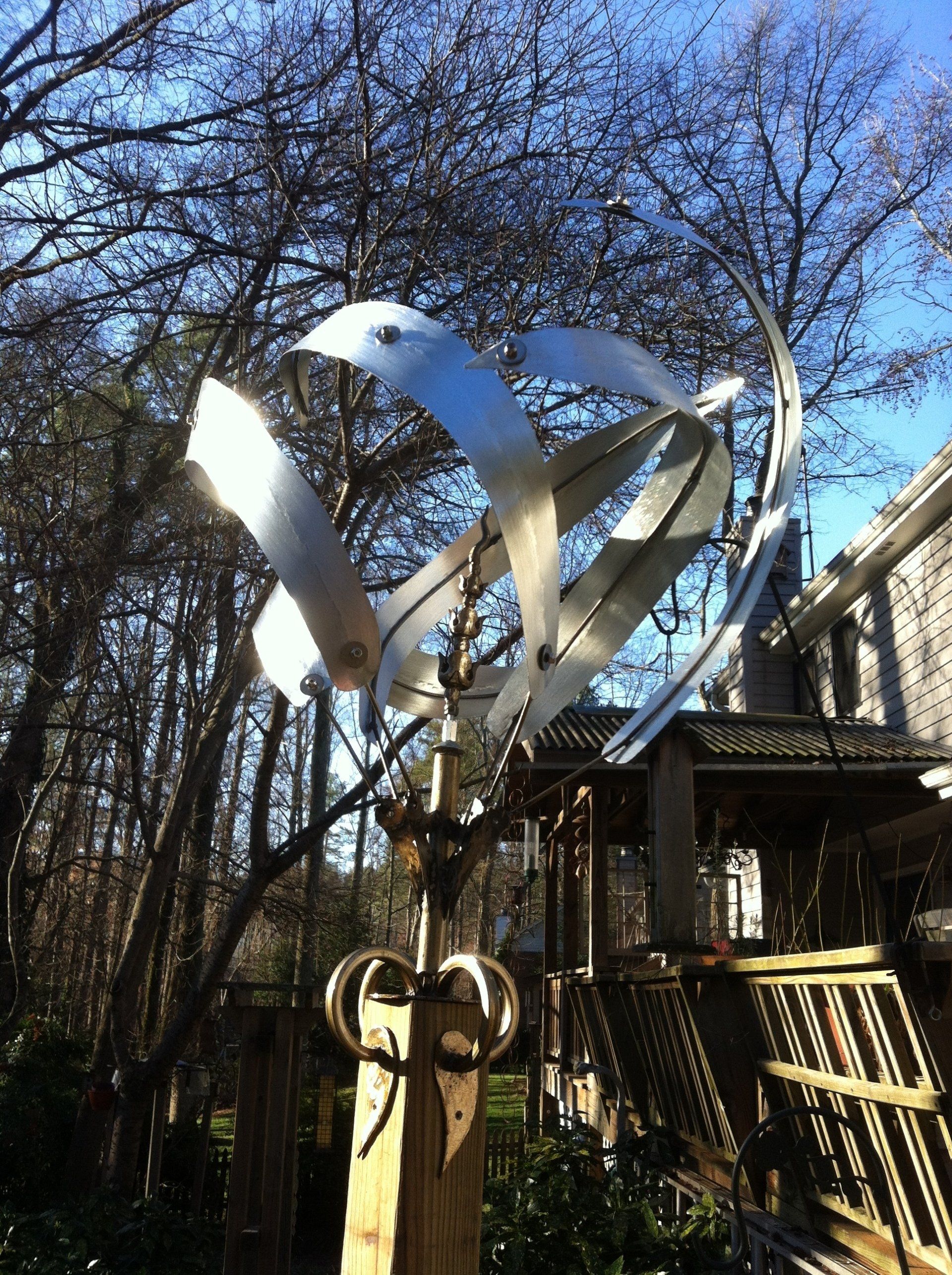 A sculpture of a bird is hanging from a tree in front of a house