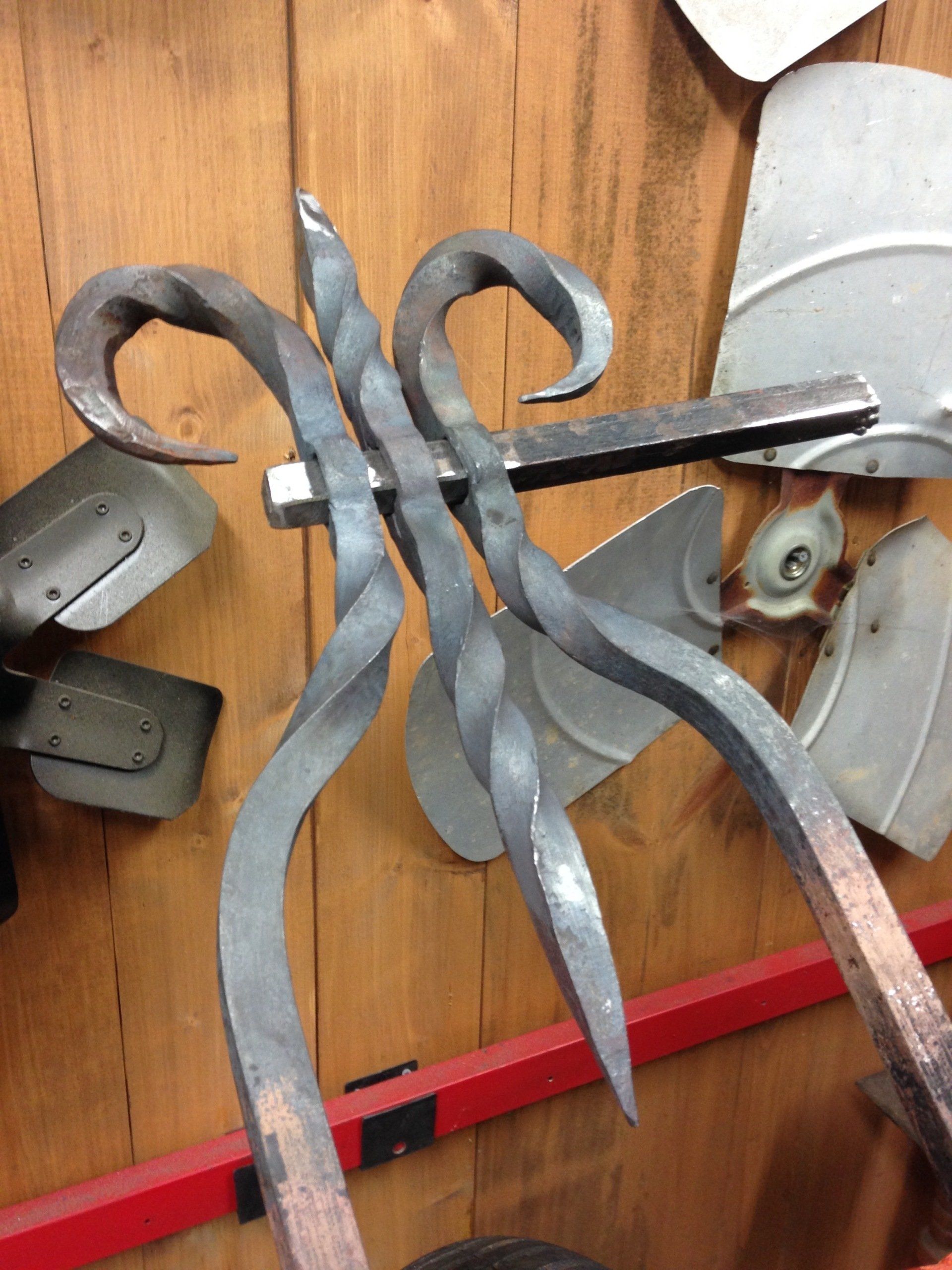 A piece of wrought iron is hanging on a wooden wall, bike sissy bar.