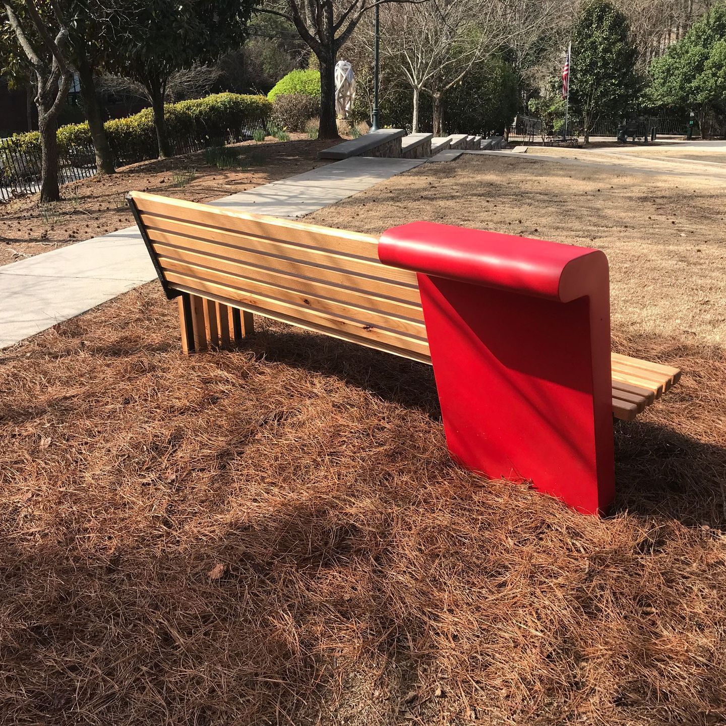 A wooden bench with a red arm rest in a park