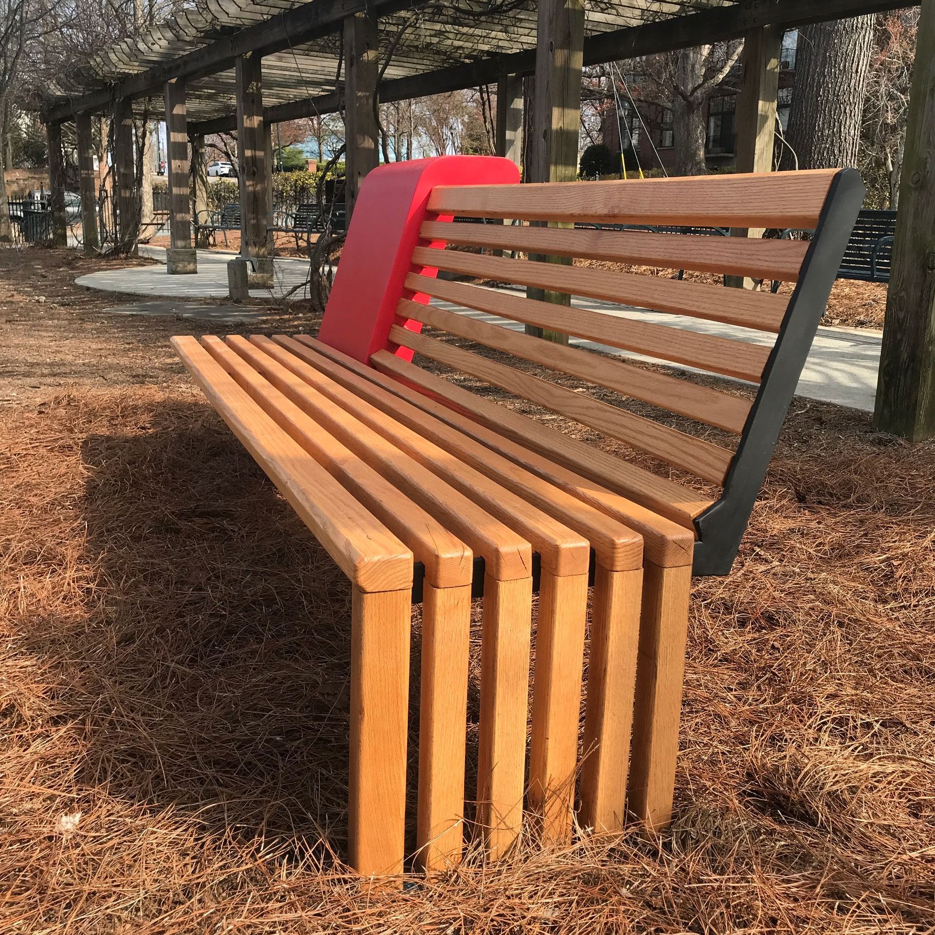 A wooden bench in a park with a red seat