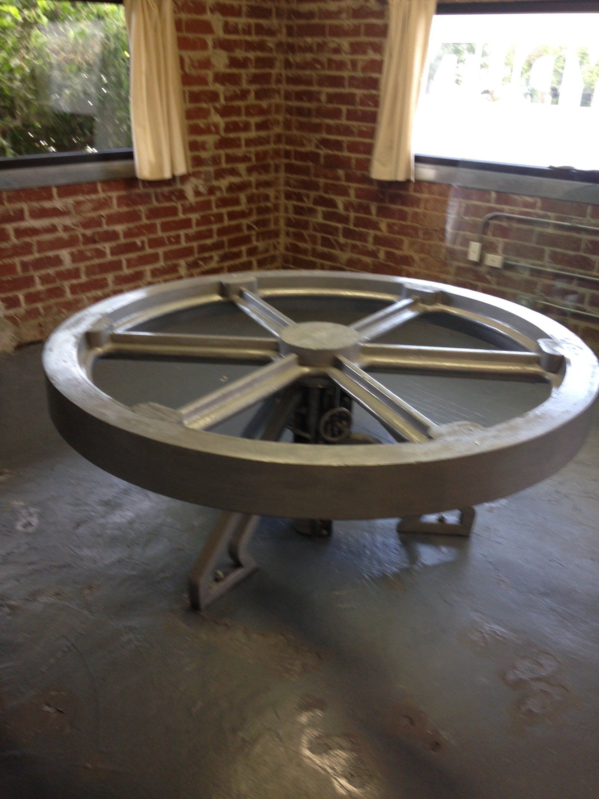 A large metal wheel is sitting in a room next to a brick wall