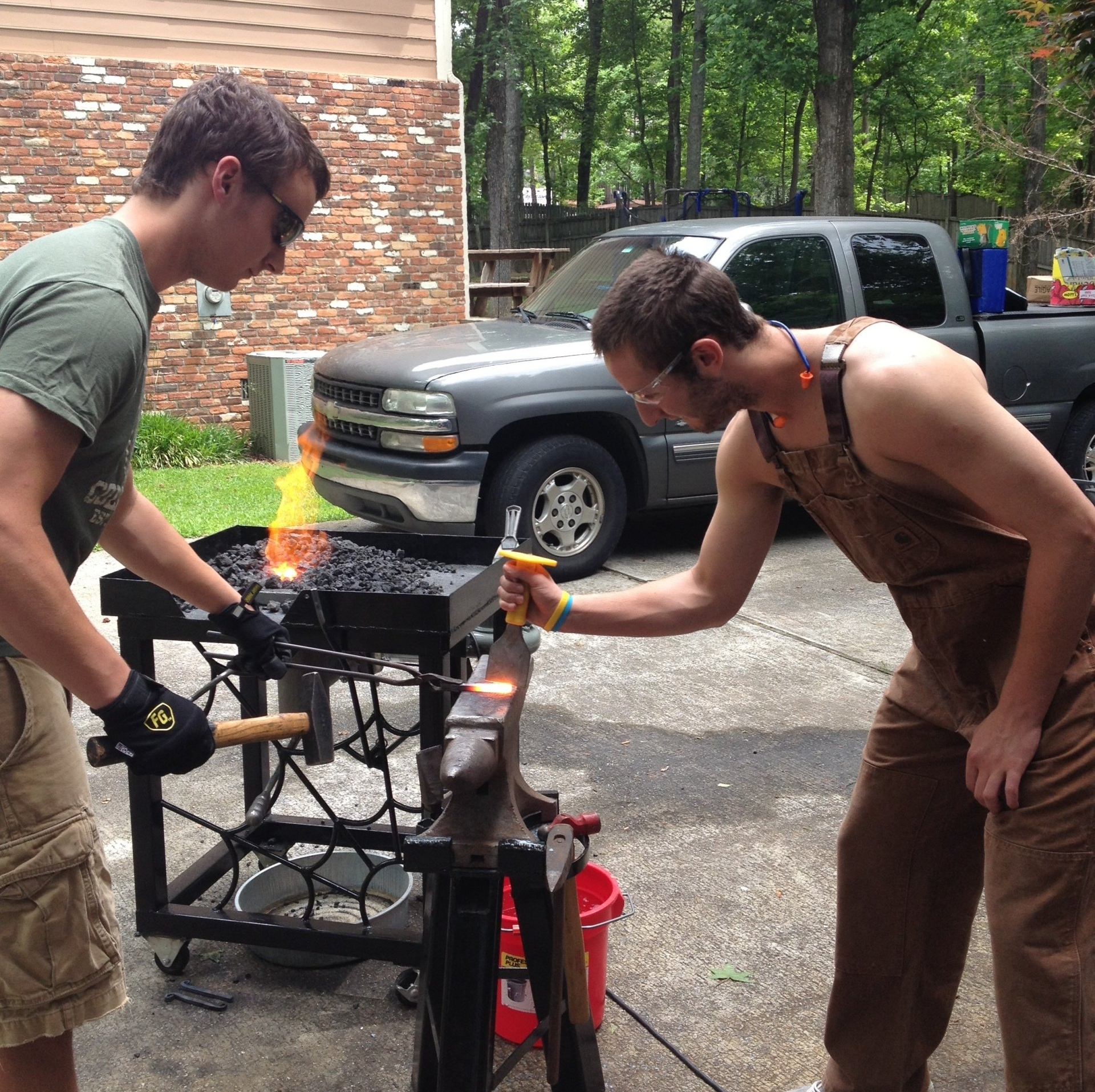 Two men are working on a piece of metal with a truck in the background