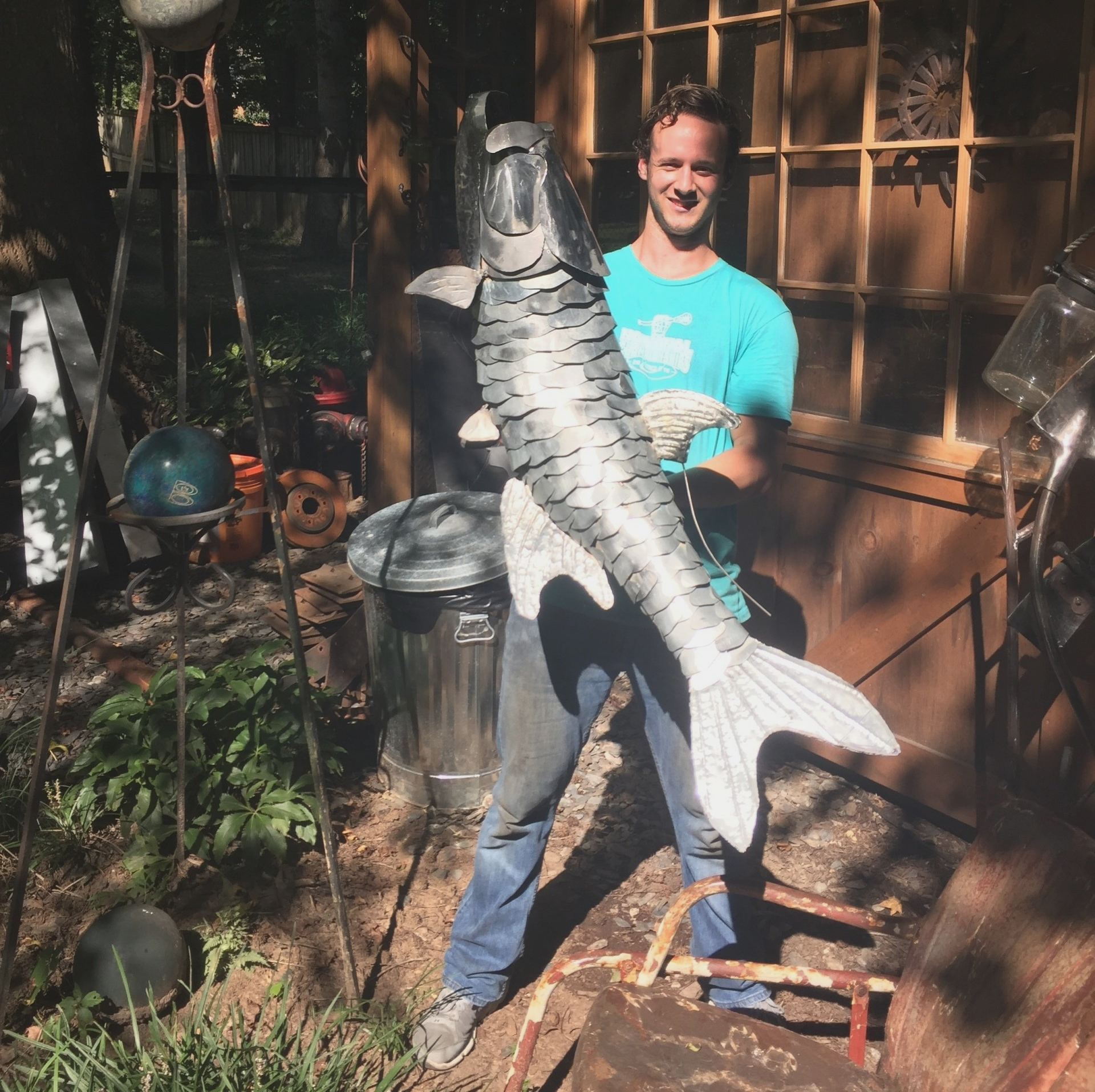 A man in a blue shirt is holding a large fish statue