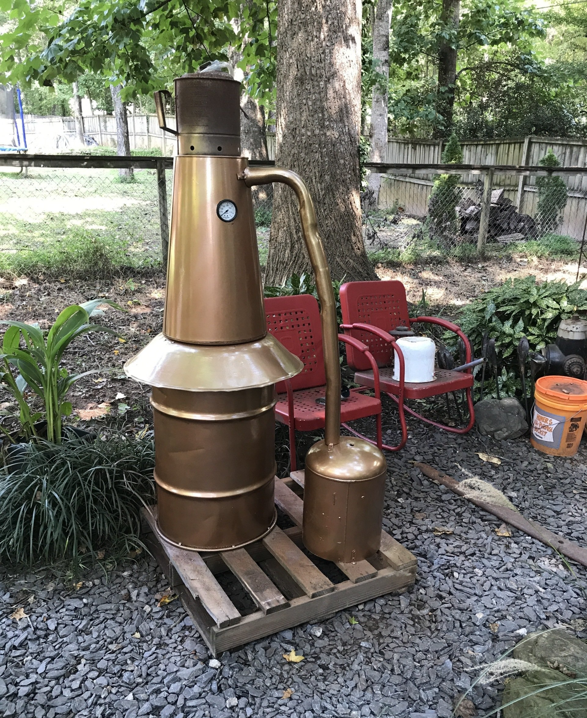 A large copper pot is sitting on top of a wooden pallet in a yard.