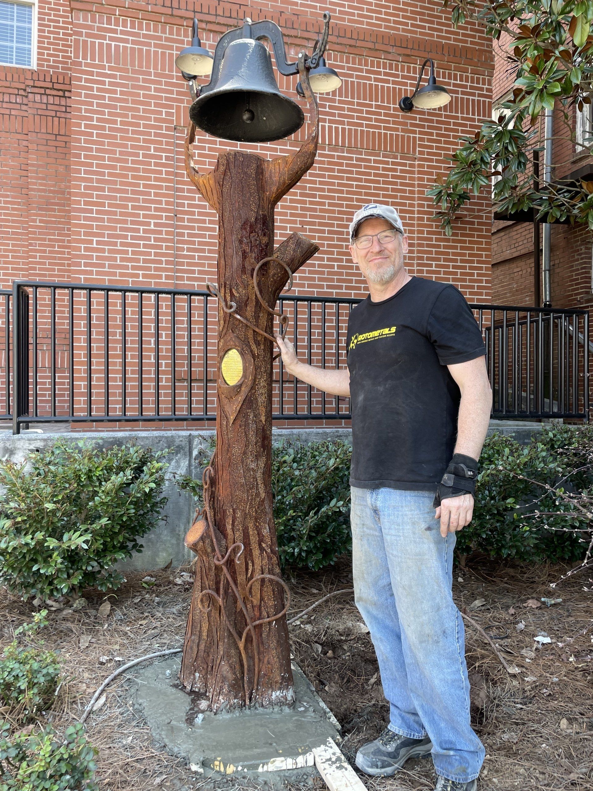 A man is standing next to a tree stump with a bell on it.