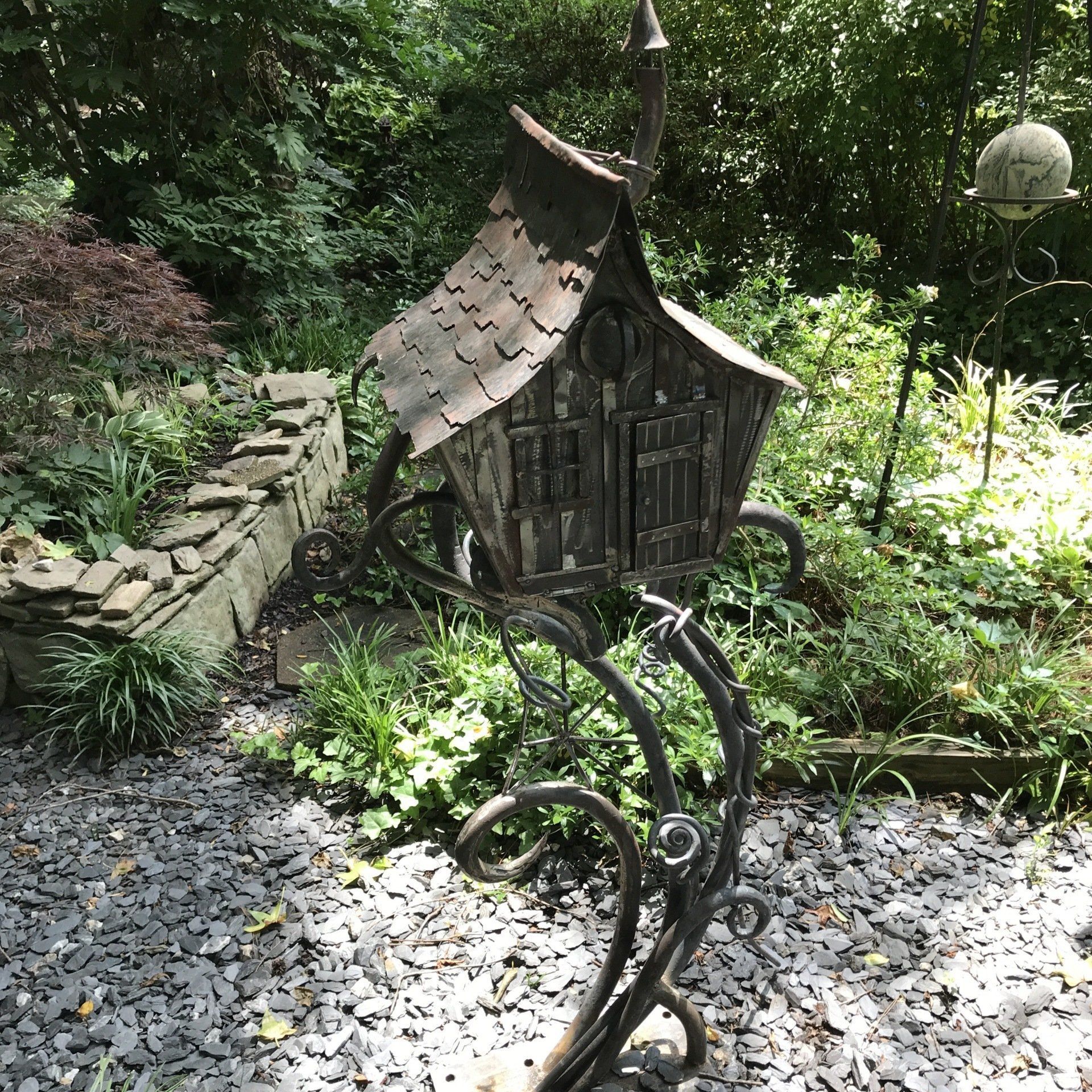 A wrought iron birdhouse is sitting on top of a pile of gravel in a garden.