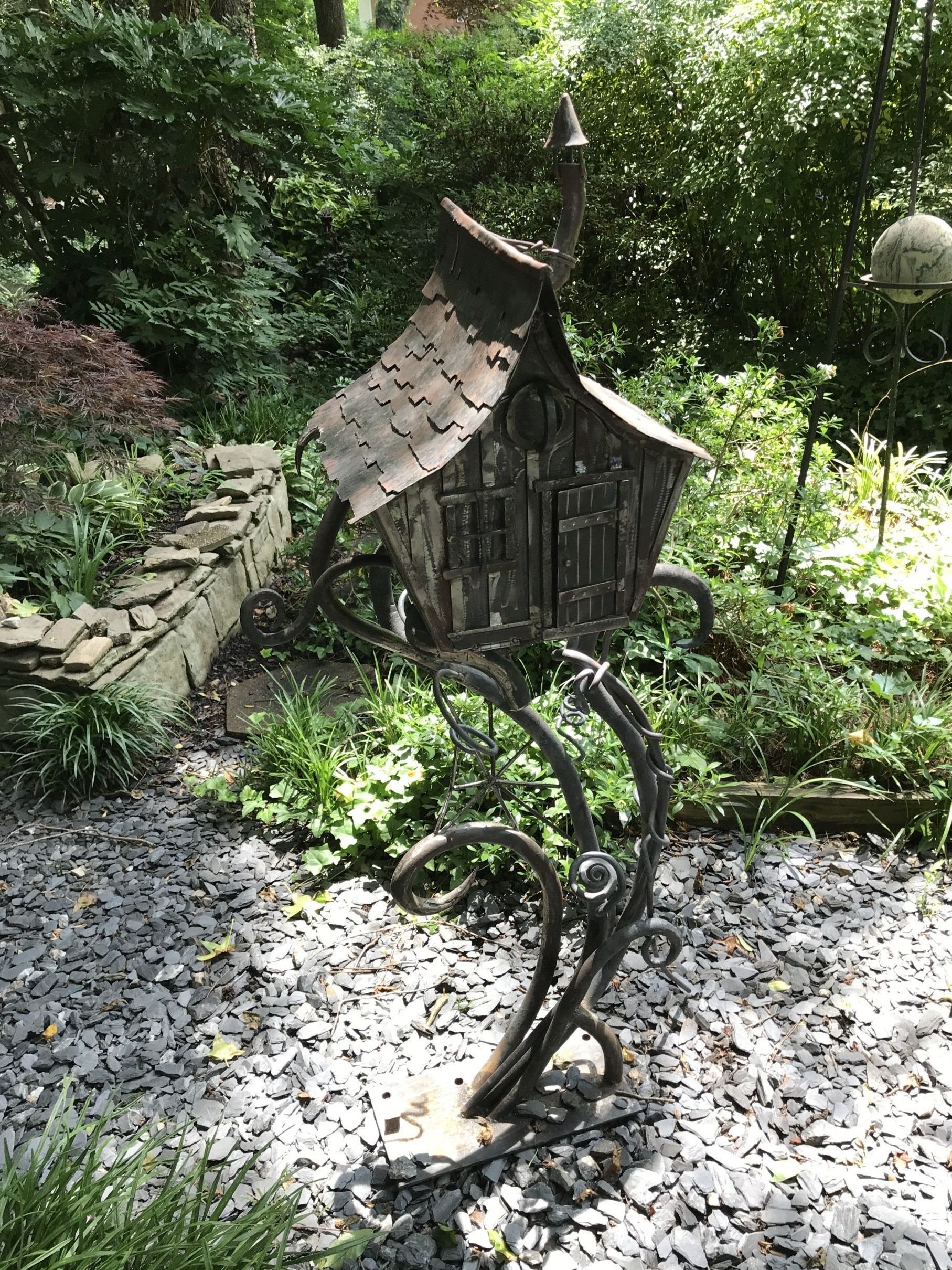 A statue of a birdhouse is sitting on top of a pile of gravel in a garden.