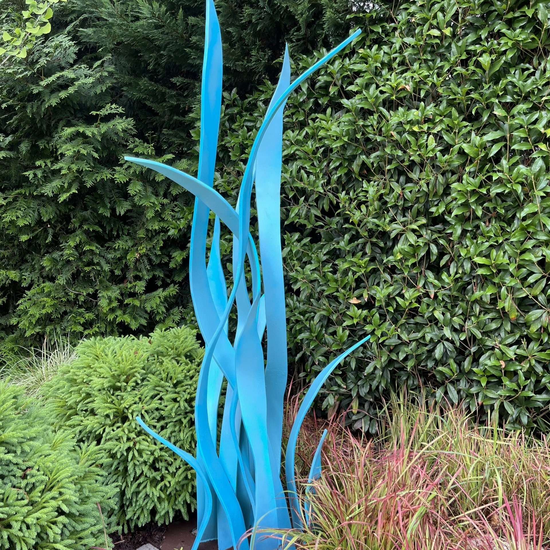 A blue sculpture is sitting in the middle of a garden.