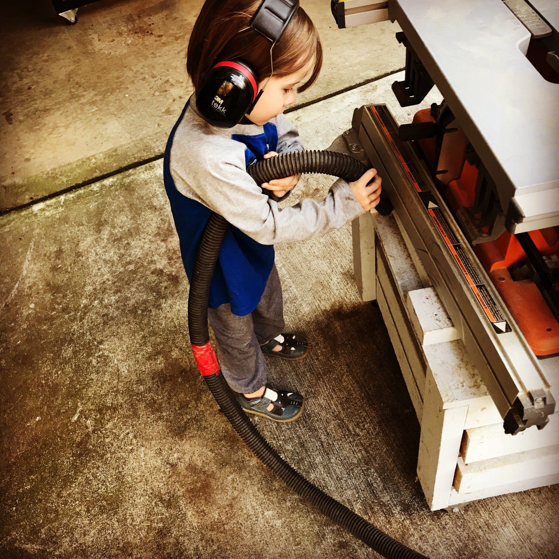A little boy wearing headphones is using a vacuum cleaner