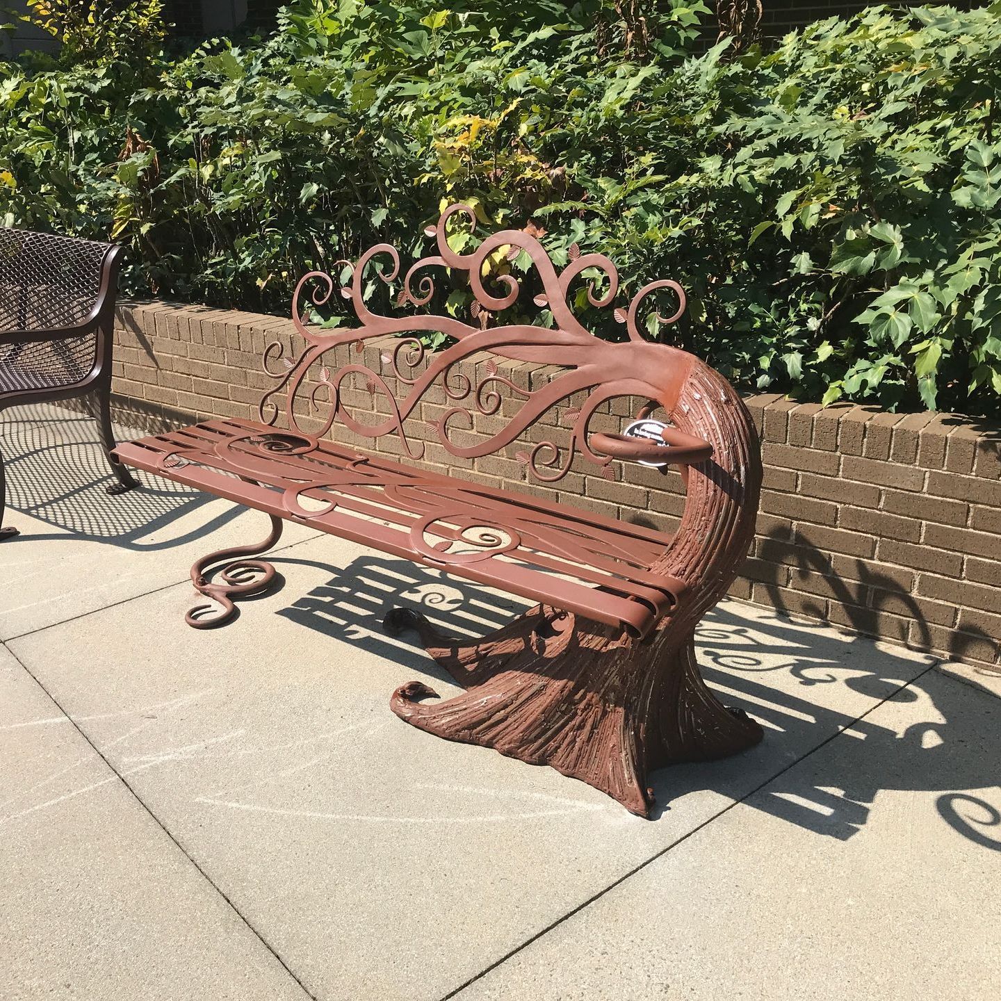 A bench with a bird on it is sitting on a sidewalk next to a brick wall.