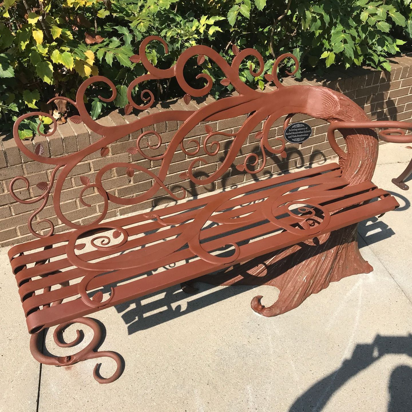 A wrought iron bench with a swirl design sits in front of a brick wall