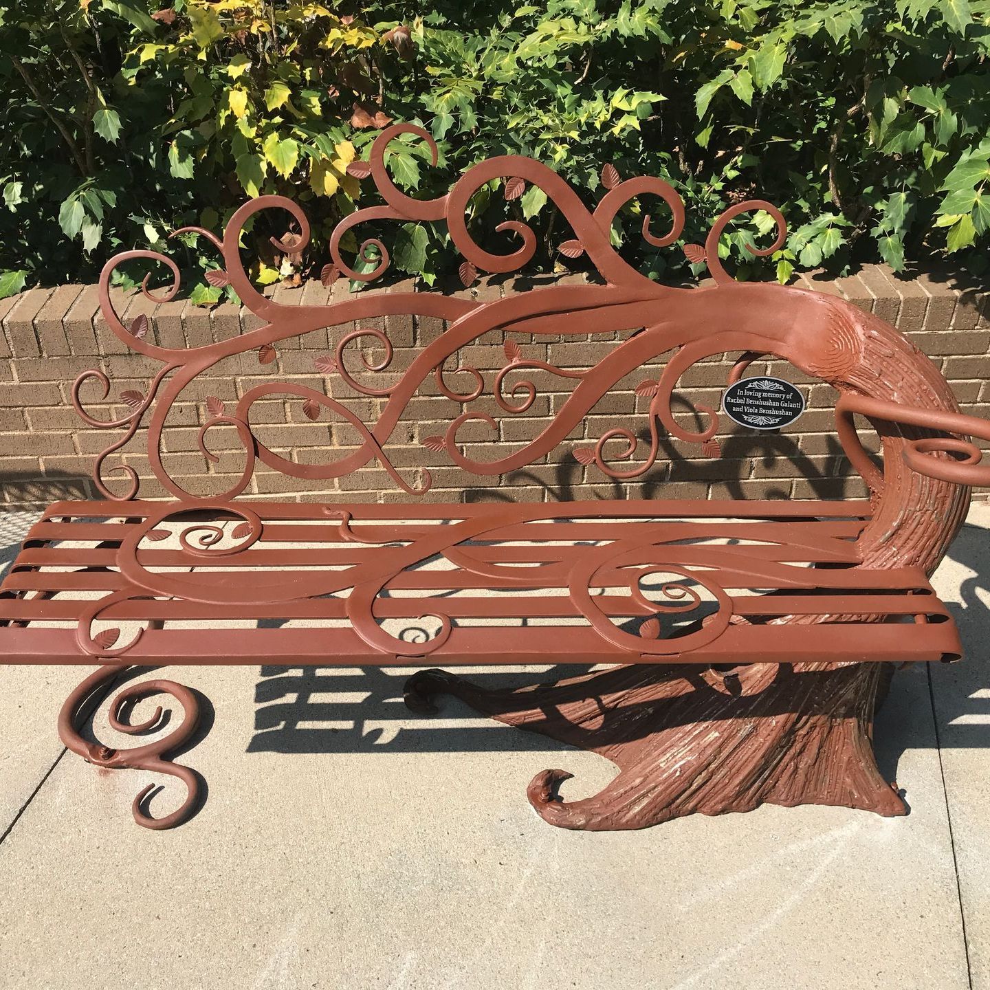 A wrought iron bench is sitting on a sidewalk in front of a brick wall