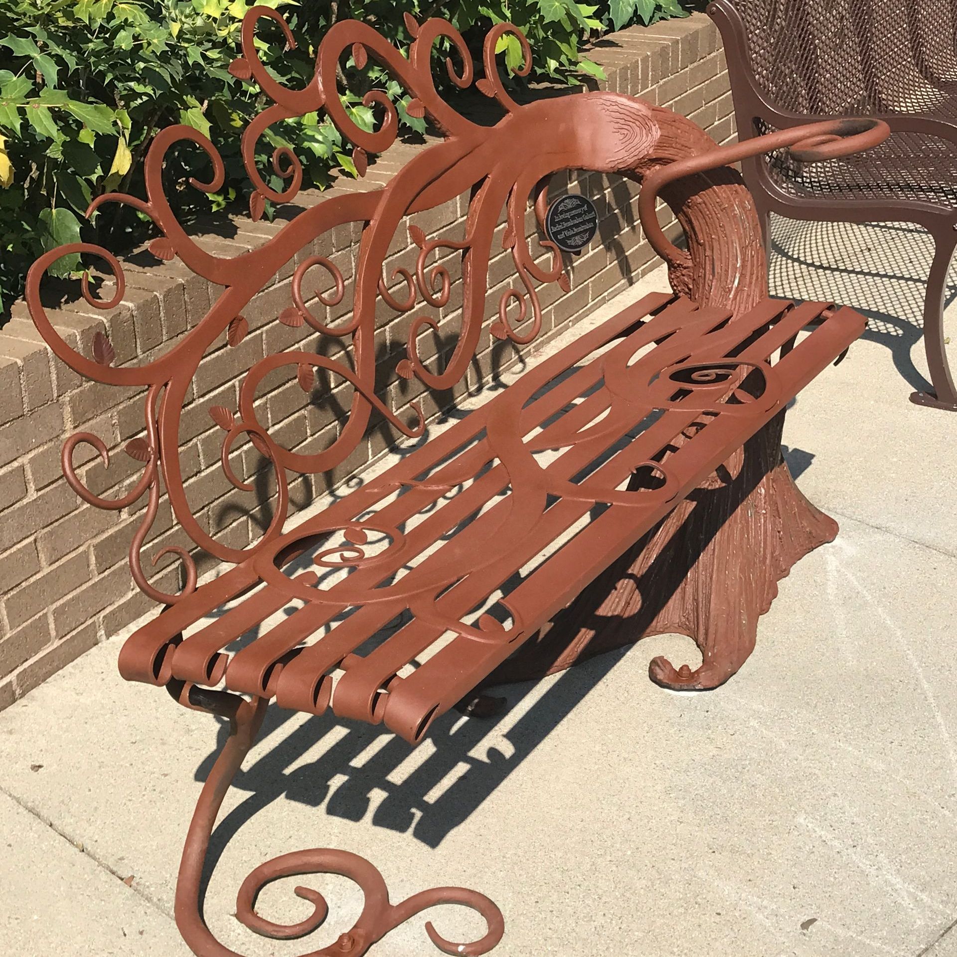 A wrought iron bench sits in front of a brick wall