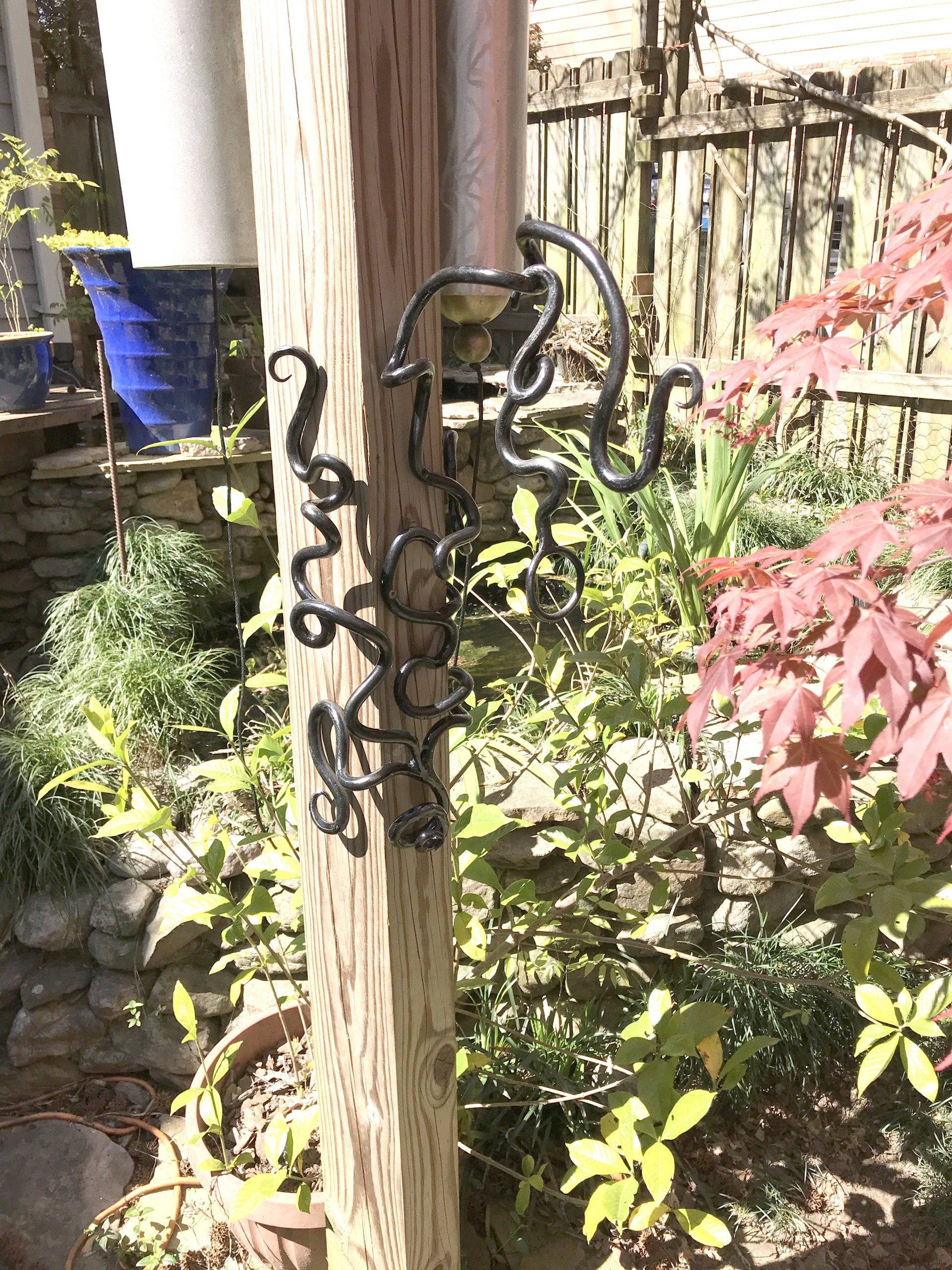A wrought iron sculpture is hanging on a wooden post in a garden.