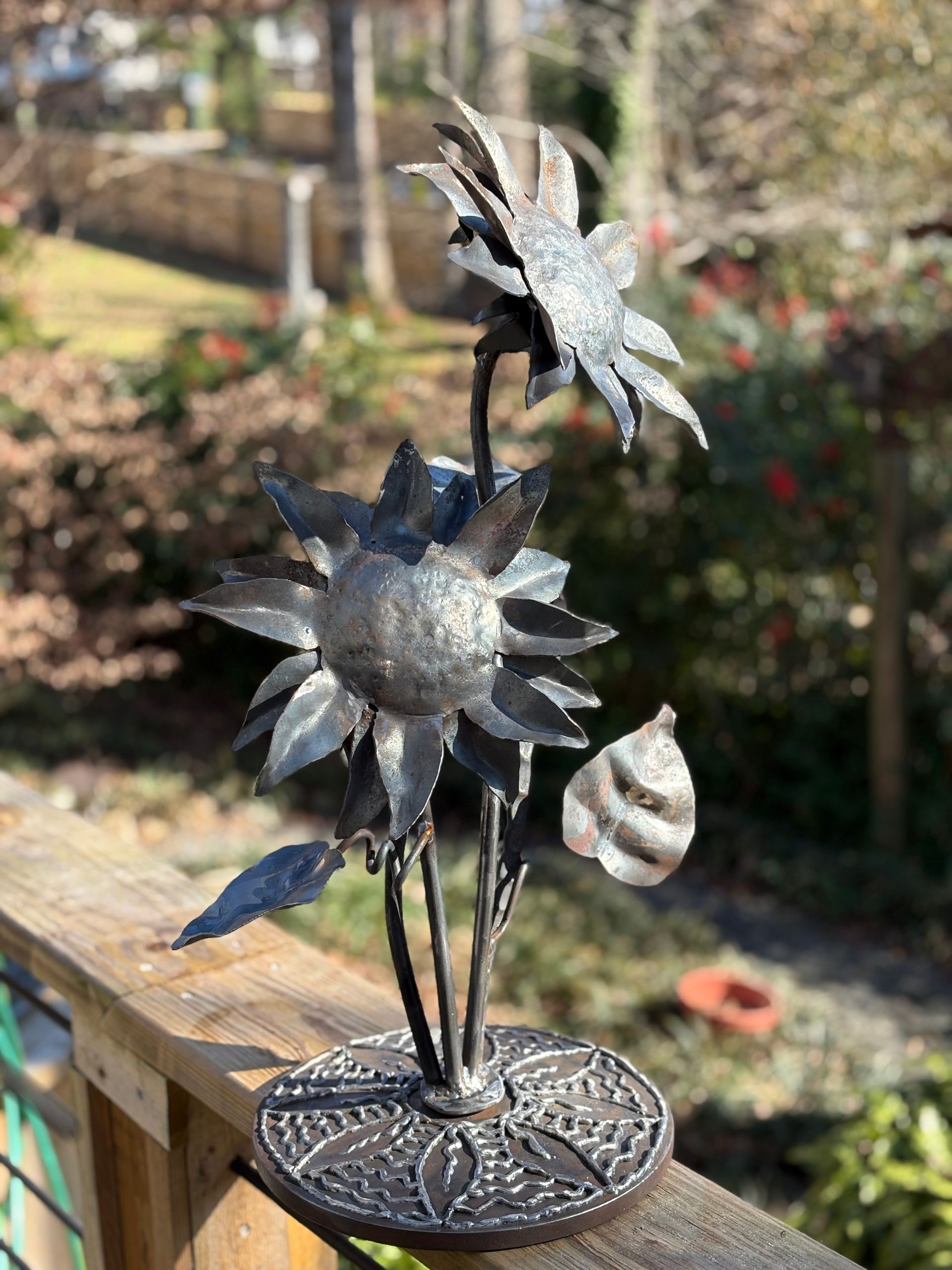 A wrought iron flower sculpture is sitting on a wooden railing.
