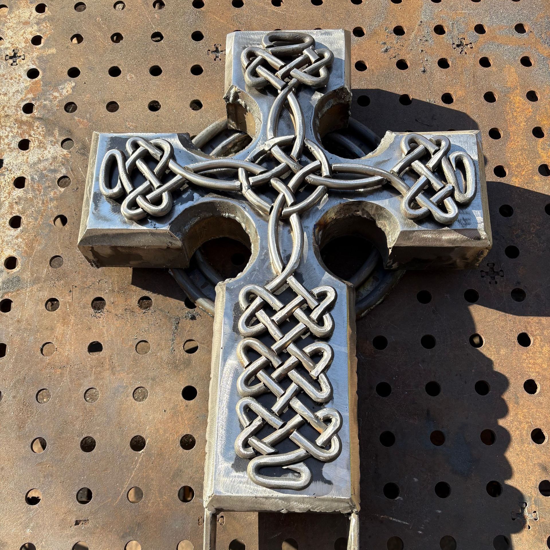 A metal cross with a celtic design is sitting on a metal surface.
