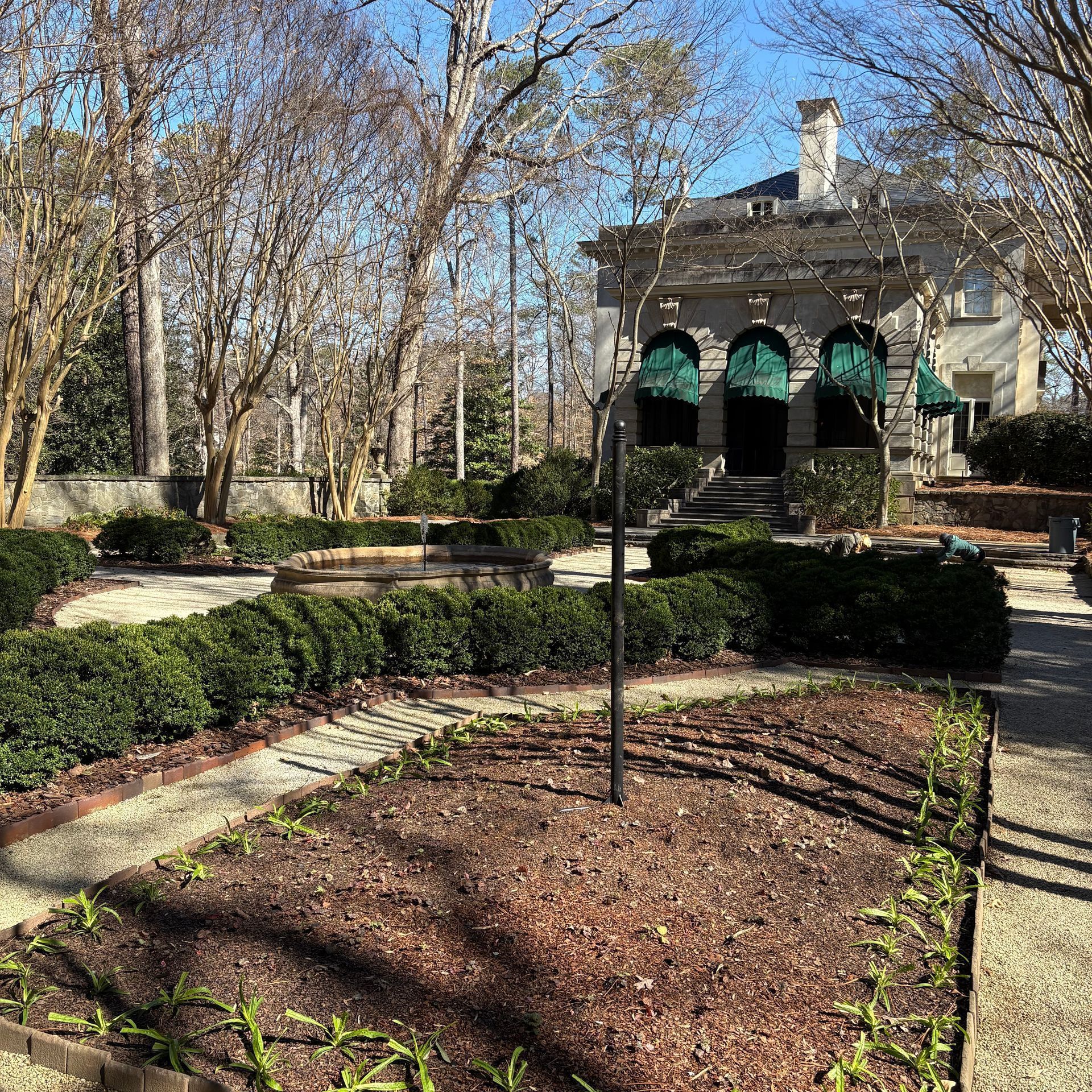 A large white house with green awnings is surrounded by trees and bushes.