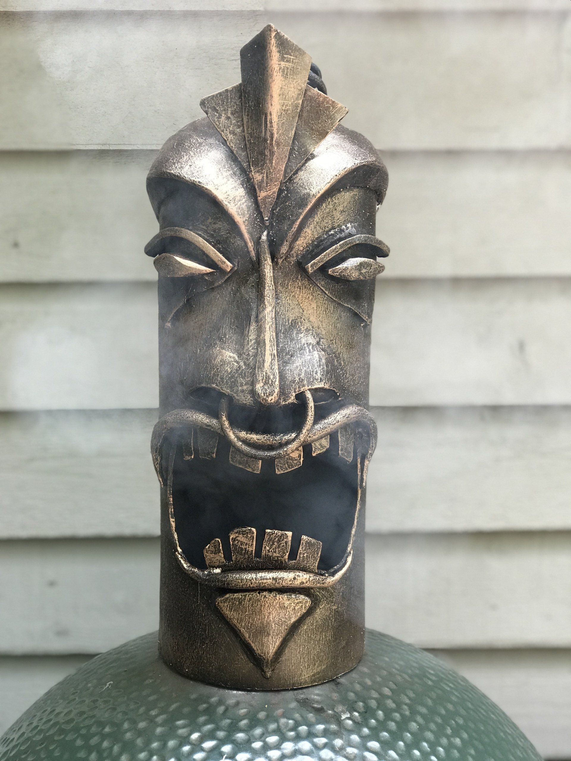 A tiki statue is sitting on top of a green egg grill
